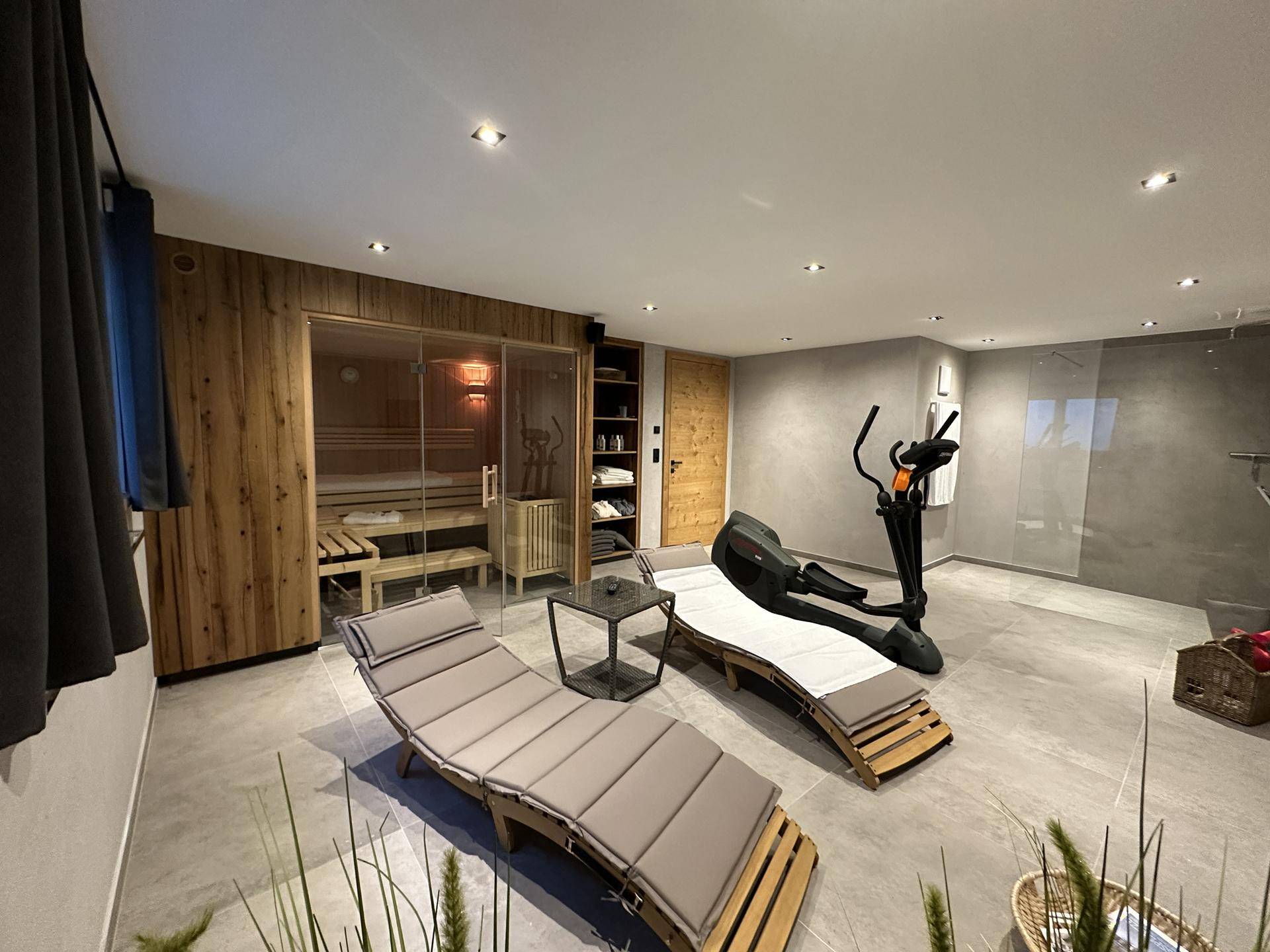 Entspannender Wellnessbereich mit Sauna, Fitnessgeräten und bequemen Liegen.