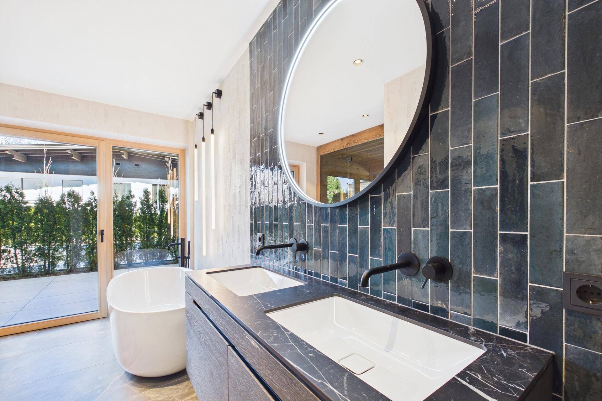 Modernes Badezimmer mit Doppelwaschbecken, freistehender Badewanne und dunklen Fliesen.