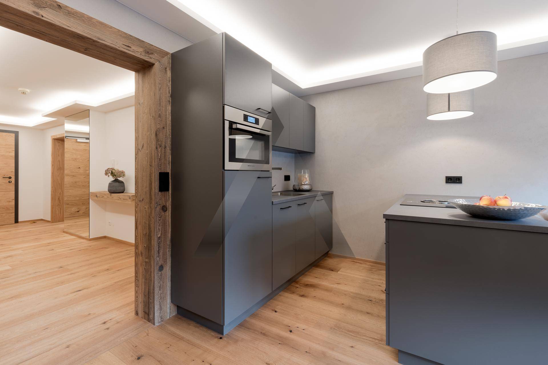 Moderne Einbauküche in Grau mit integrierten Geräten und Holzboden, offen zum Flur.