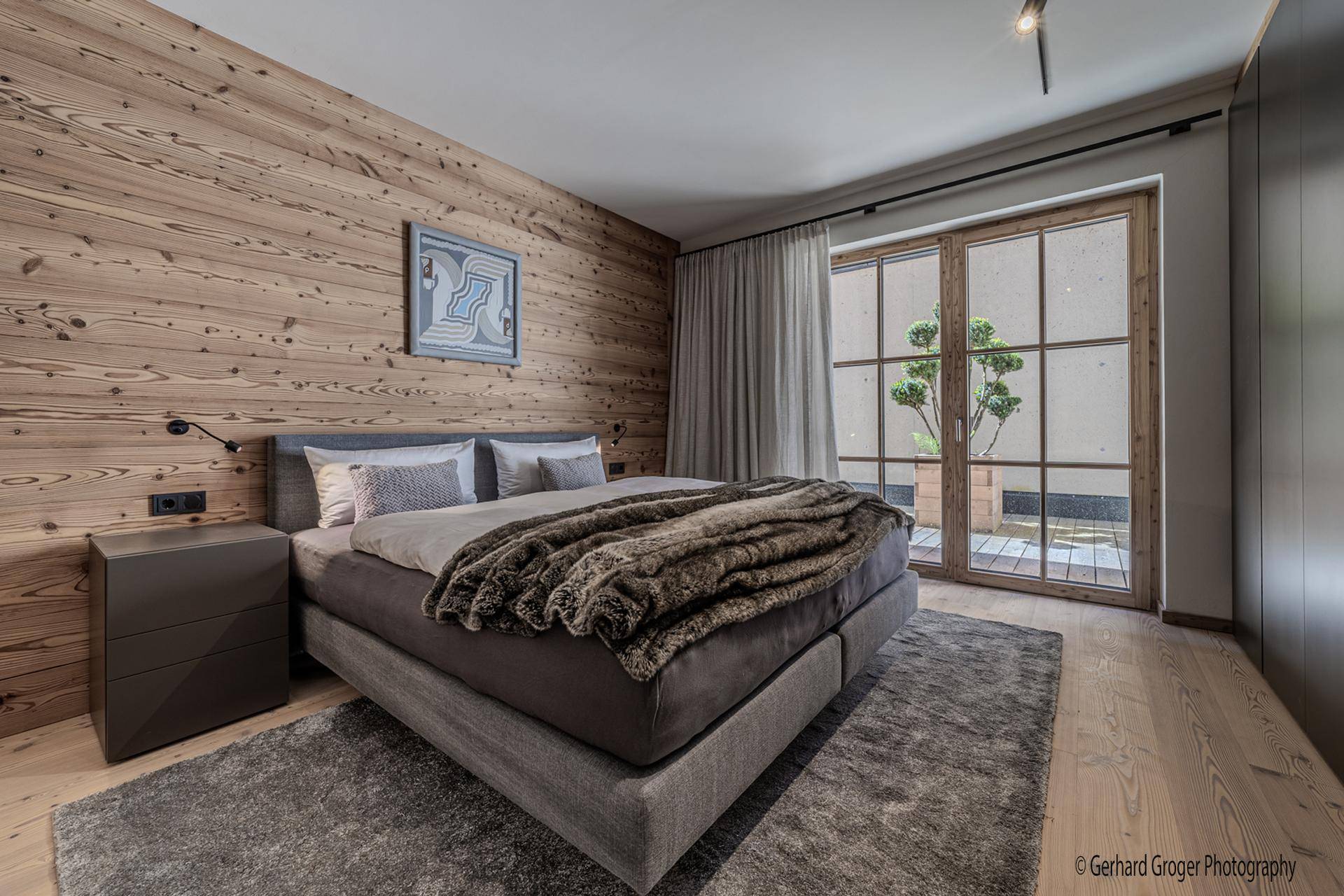 Schlafzimmer mit Holzwand, großem Bett und Zugang zu einem kleinen Außenbereich.