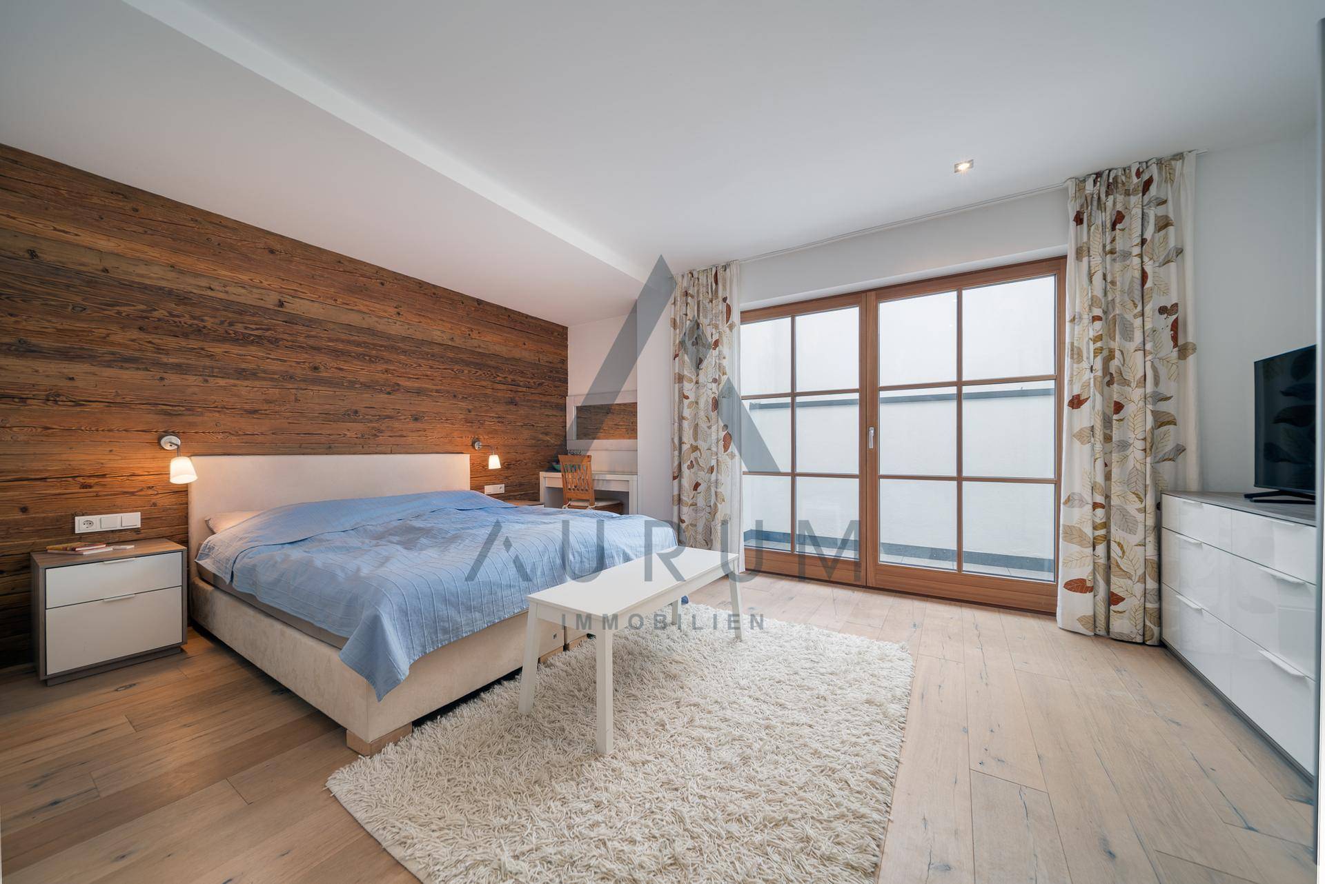 Schlafzimmer mit Holzwand, Parkettboden und Zugang zu einem Balkon.