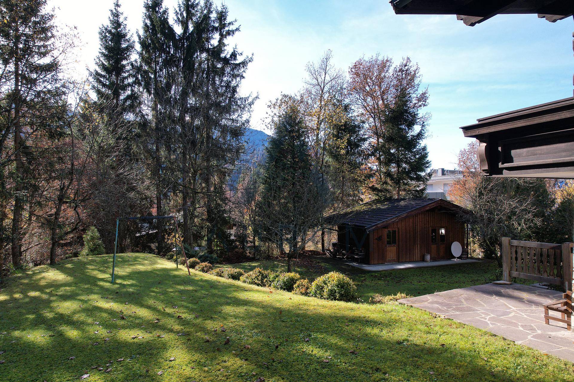 Weitläufiger Garten mit Rasen, Bäumen und einem kleinen Holzhaus im Hintergrund.