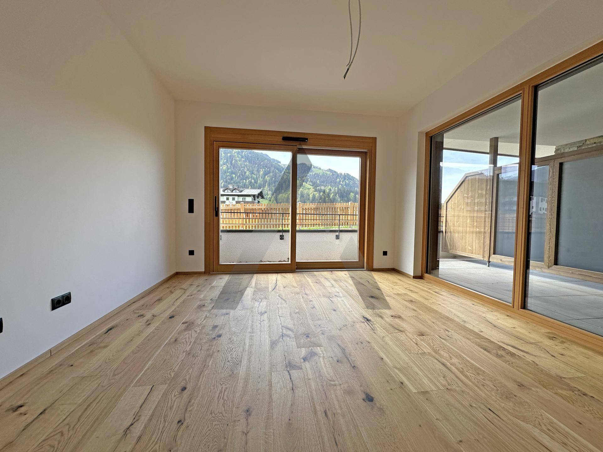 Helles Zimmer mit Holzboden und großen Schiebetüren, die Zugang zu einem Balkon bieten.