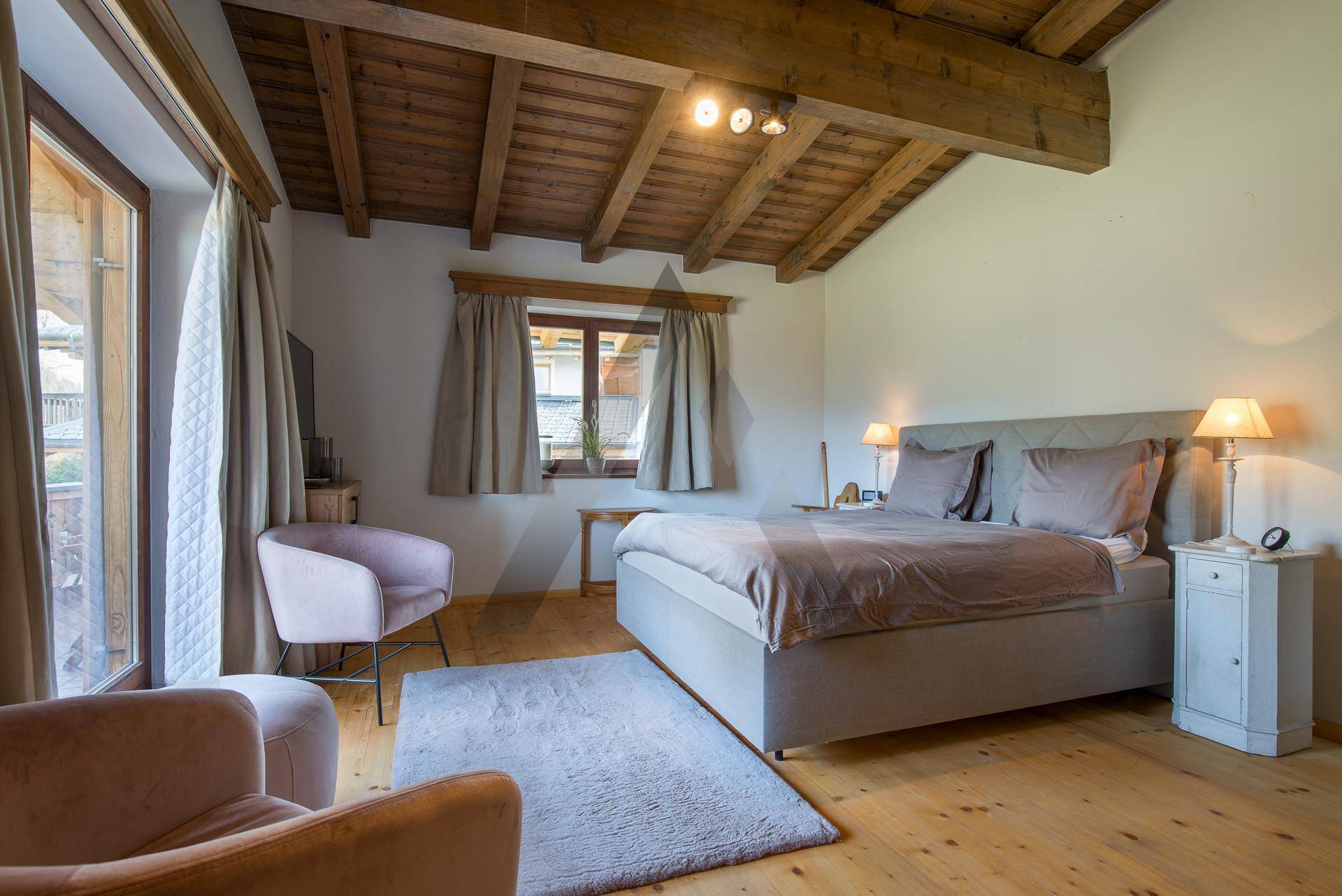 Gemütliches Schlafzimmer mit Holzboden, sichtbaren Deckenbalken und direktem Balkonzugang.