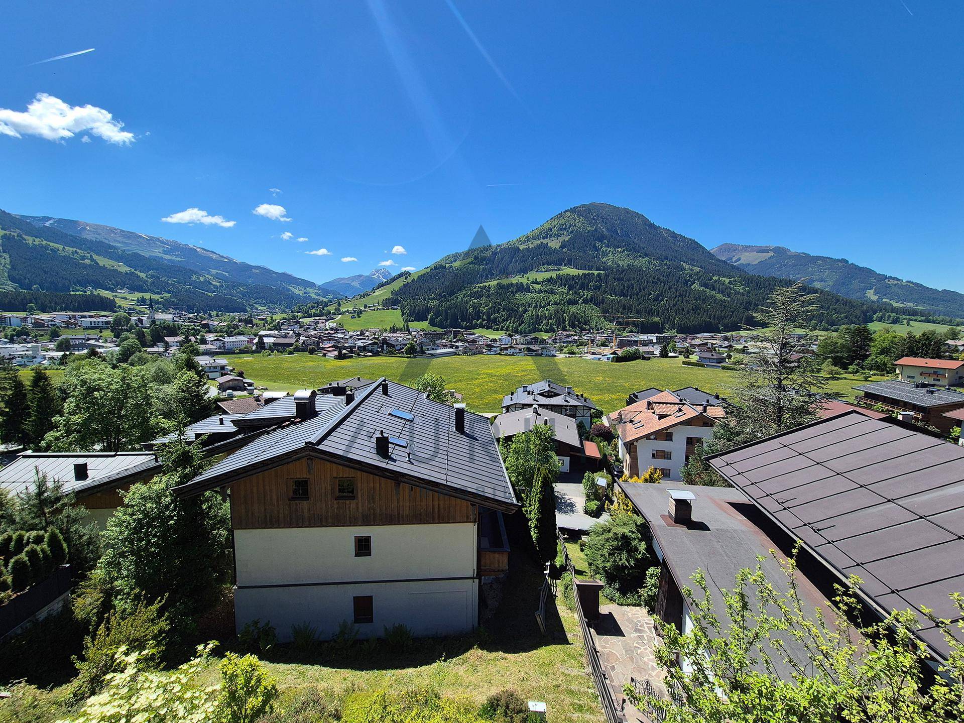 Panoramablick über eine Wohnsiedlung mit traditionellen Häusern, umgeben von grünen Wiesen und Bergen.