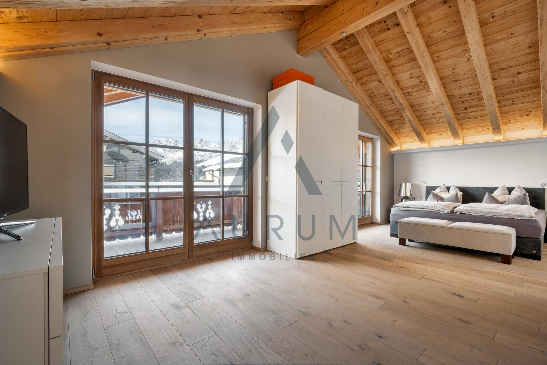 Schlafzimmer im Dachgeschoss mit Holzbalken, Bergblick und Zugang zum Balkon.
