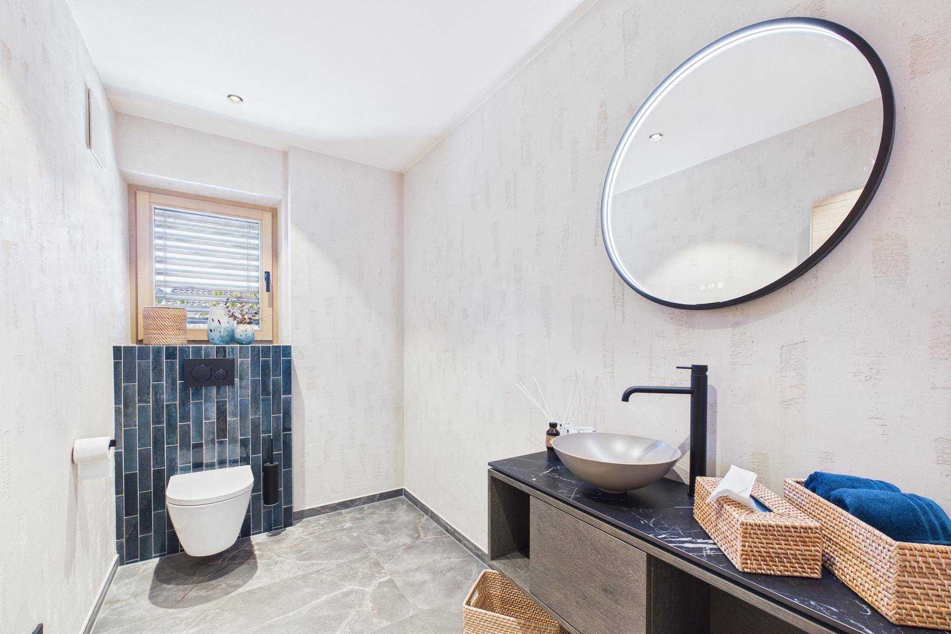 Modernes Gäste-WC mit stilvollem Waschbecken, beleuchtetem Spiegel und Fenster.
