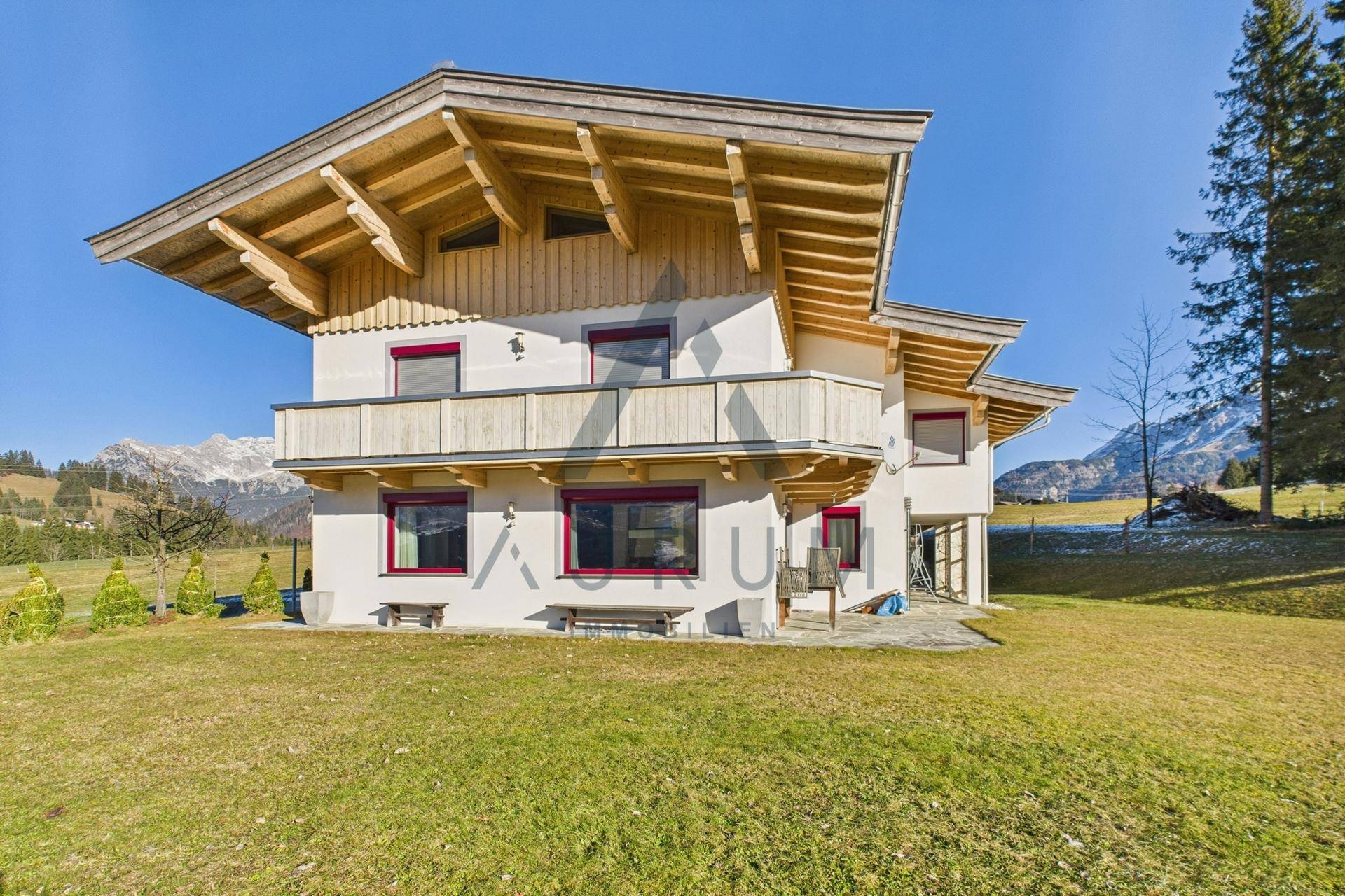 Charmantes Haus im Alpenstil mit Holzbalkonen, umgeben von einer gepflegten Rasenfläche und Bergen.