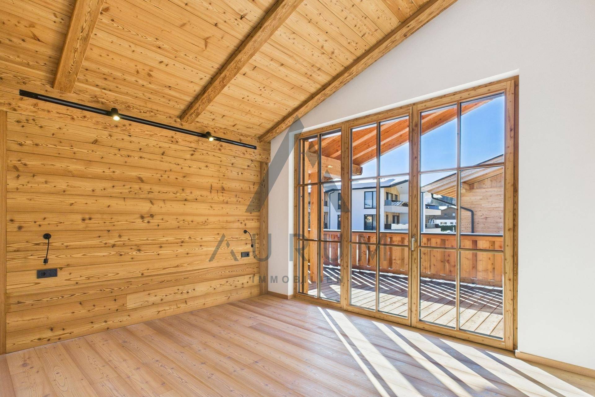 Leerer Raum mit Holzwänden, Dachschräge und großen Fenstern mit Zugang zu einem Balkon.