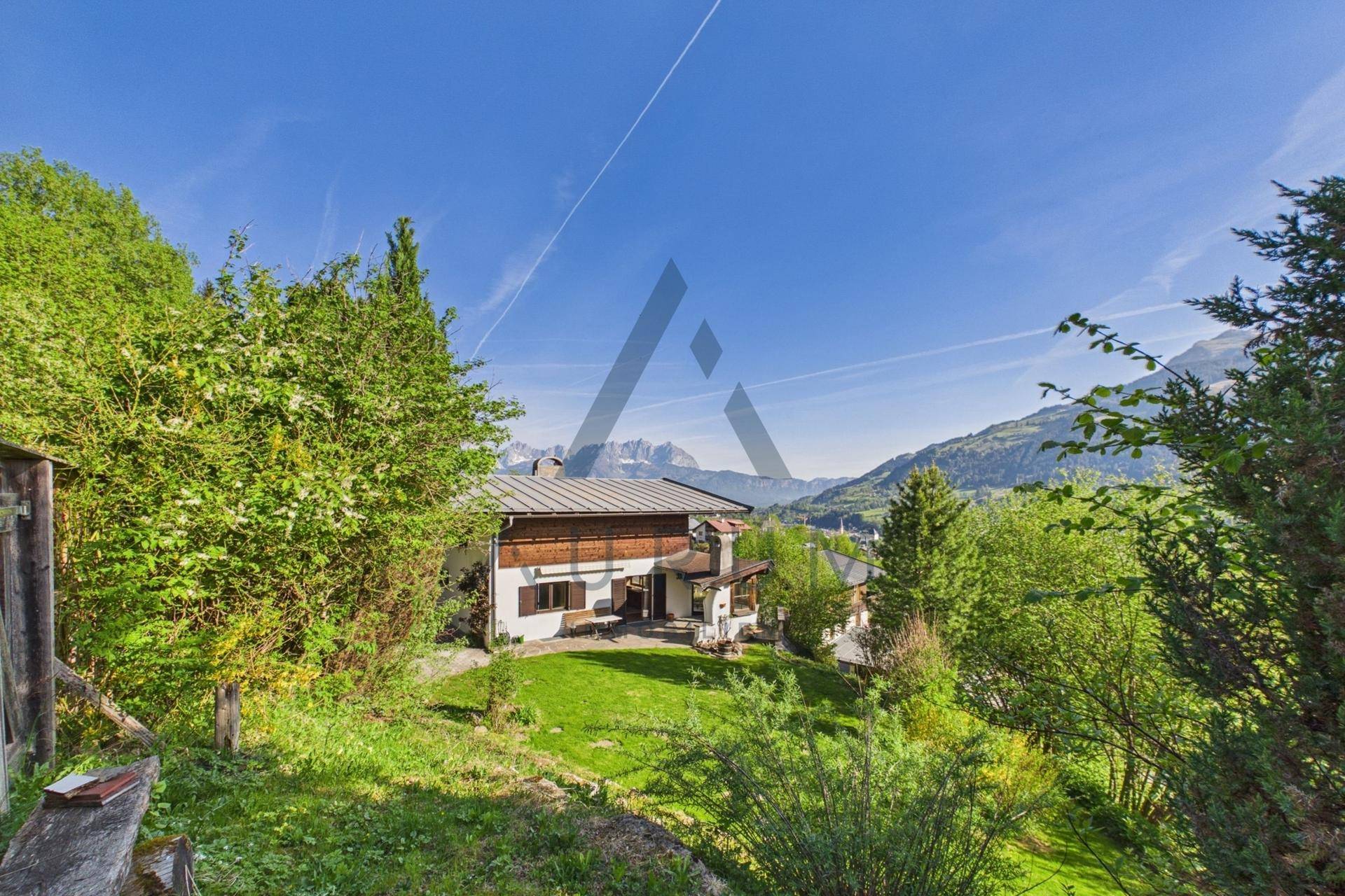 Großzügiger Gartenbereich mit Rasenfläche und einem charmanten Haus im alpinen Stil, umgeben von Bergen.