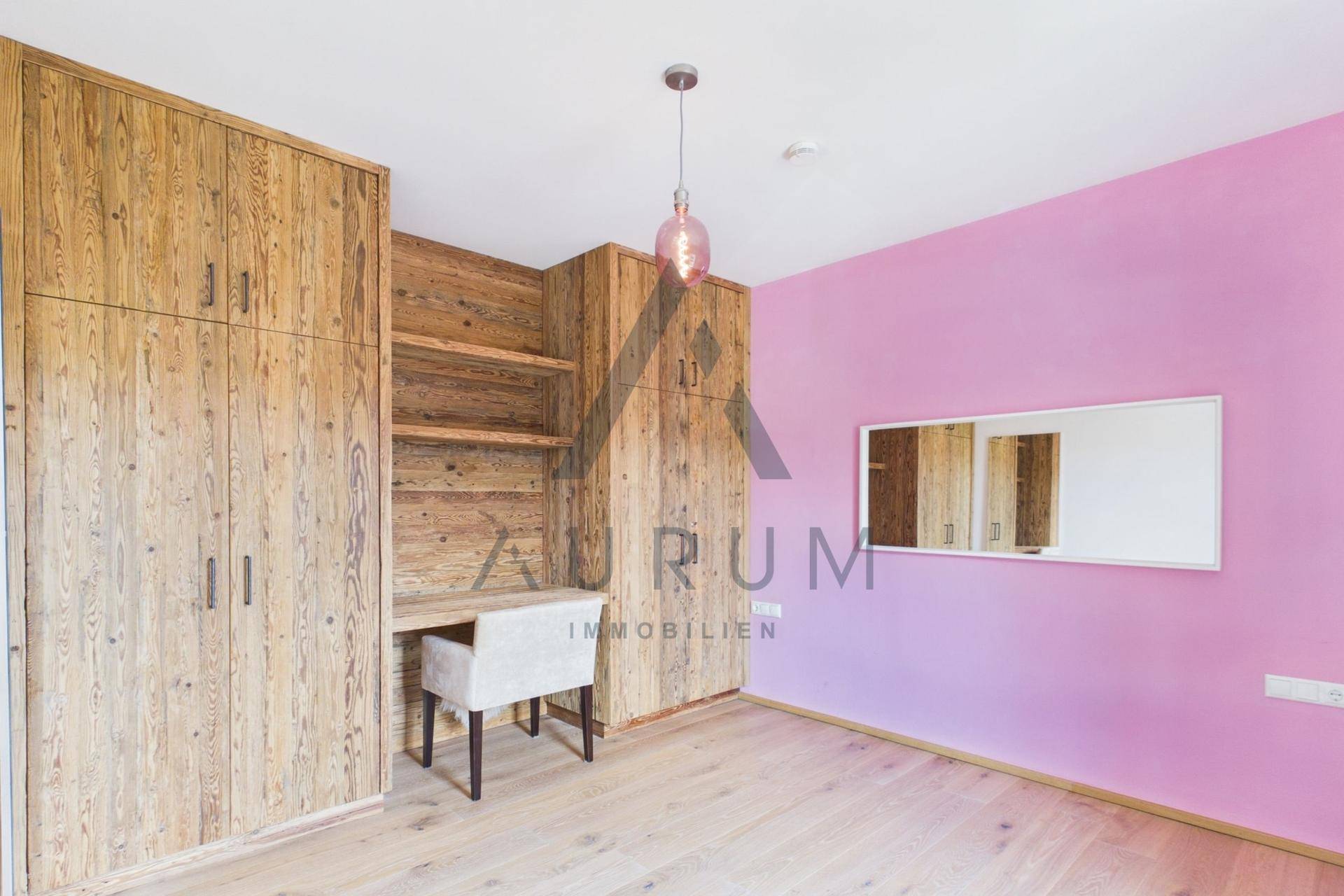 Schlafzimmer mit maßgefertigten Holzschränken, Schreibtisch und rosa Akzentwand.
