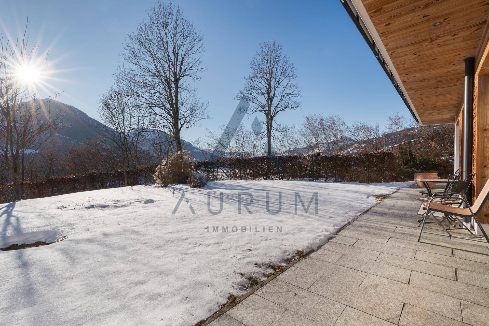 Weitläufiger Gartenbereich mit gepflasterter Terrasse, umgeben von Schnee und mit Blick auf die Berge.