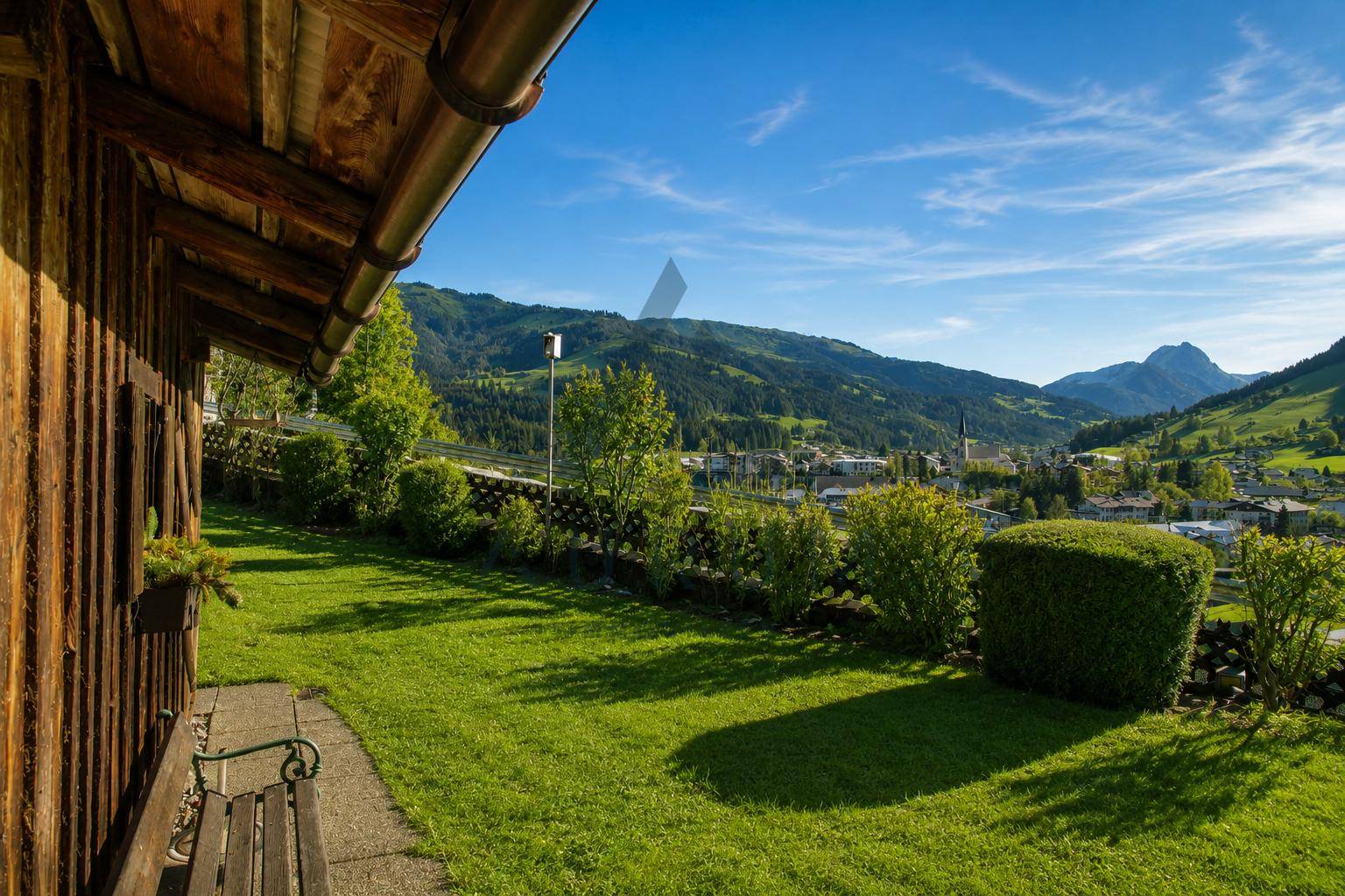 Gemütlicher Gartenbereich mit Holzbank und Blick auf das Dorf sowie die grüne Berglandschaft.