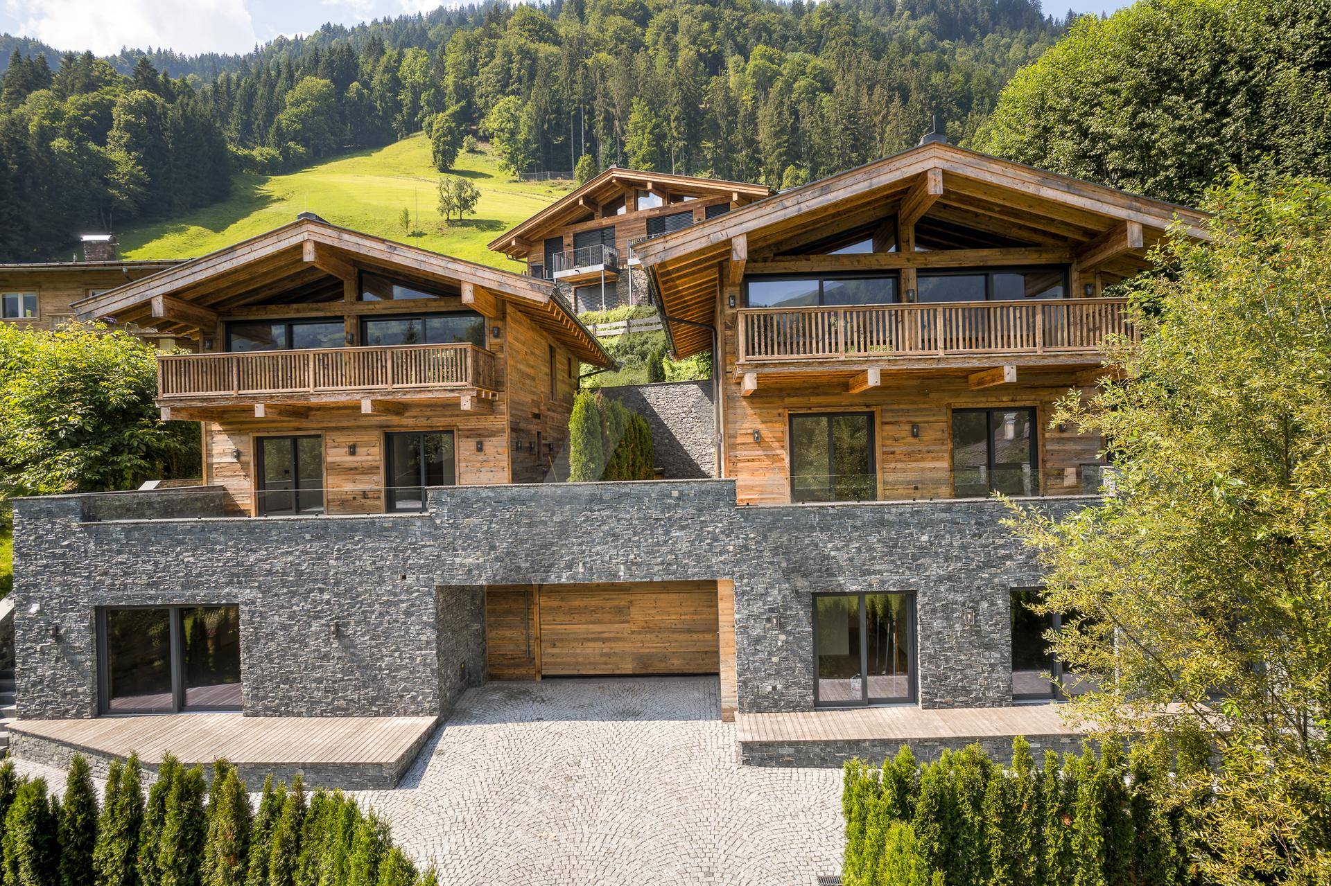 Mehrere moderne Chalets mit Steinfassaden und Holzelementen in einer Berglandschaft mit Garageneinfahrt.