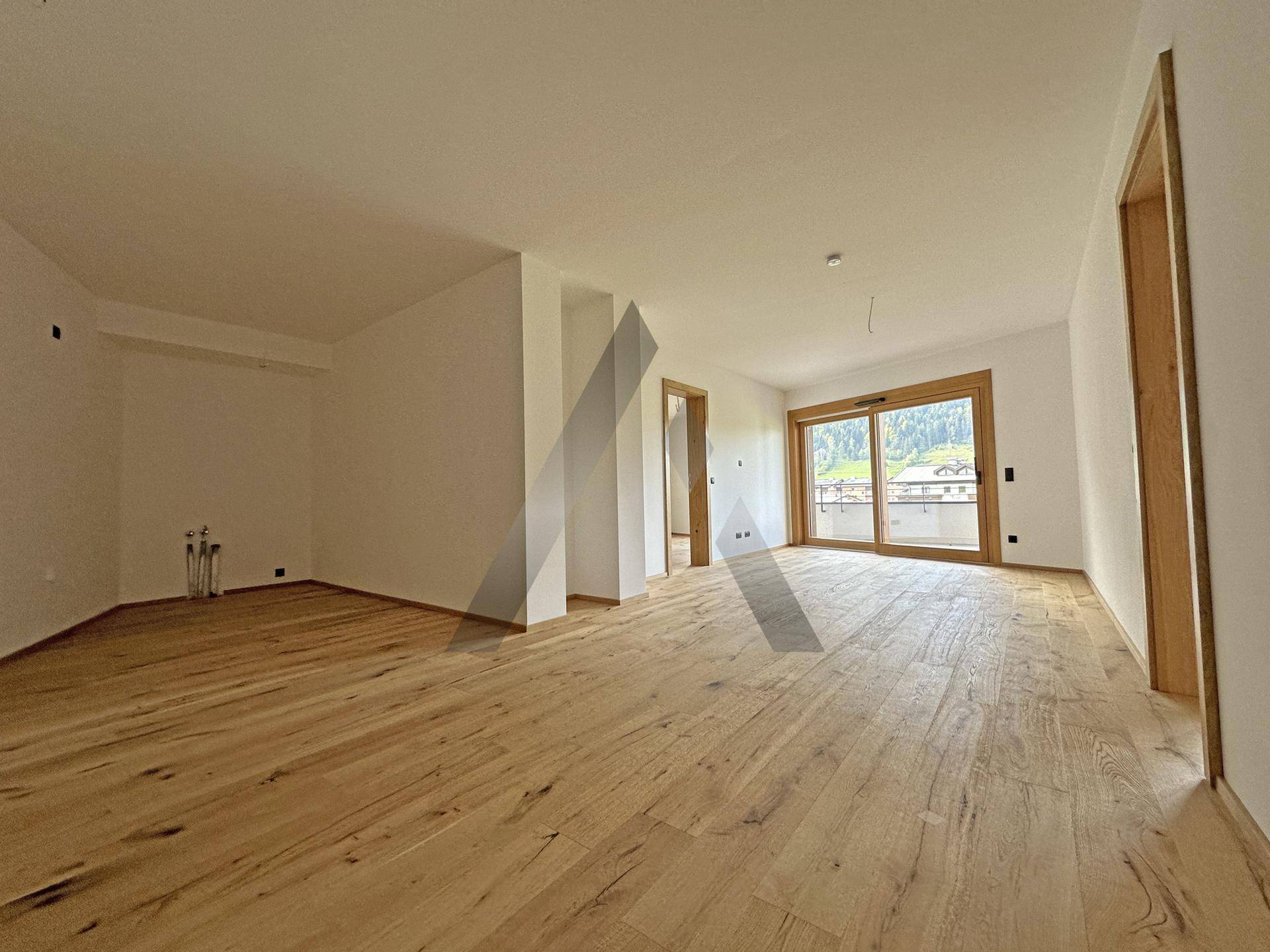 Heller, offener Raum mit Holzboden und Zugang zu einem Balkon, ideal für Wohn- oder Essbereich.