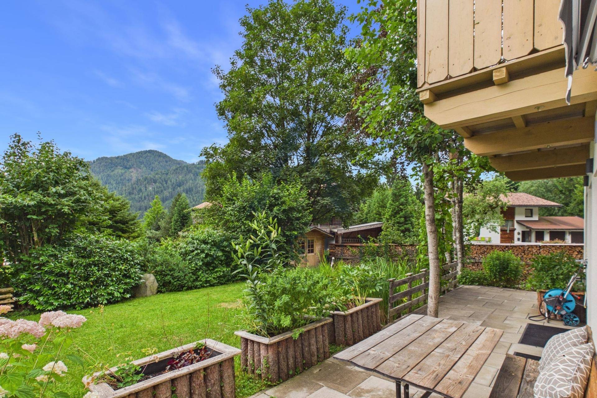 Großer Gartenbereich mit Terrasse, Holztisch und Blick auf die Berge.