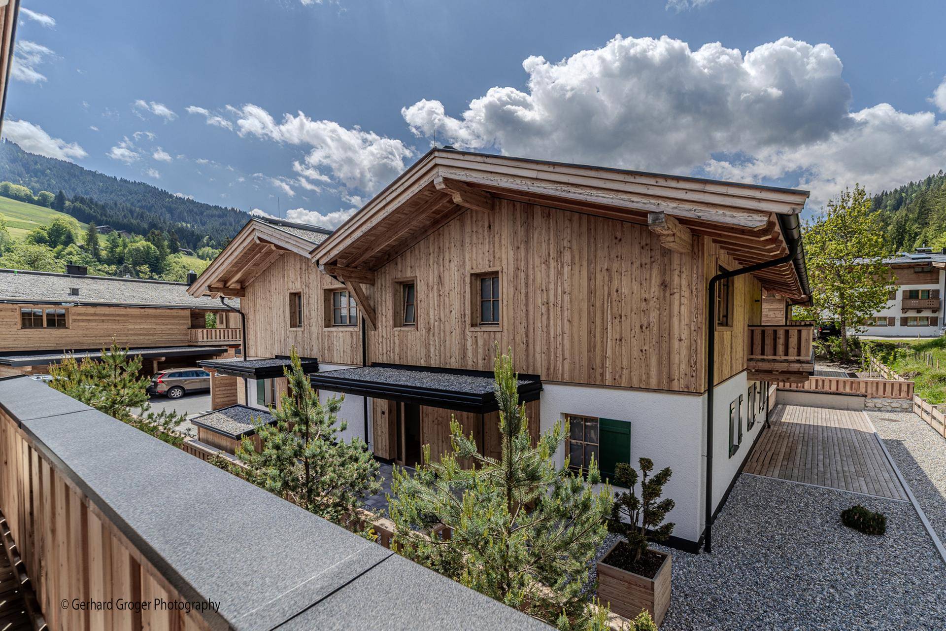Rückansicht eines modernen Holzchalets mit Parkplatz und grüner Bepflanzung.