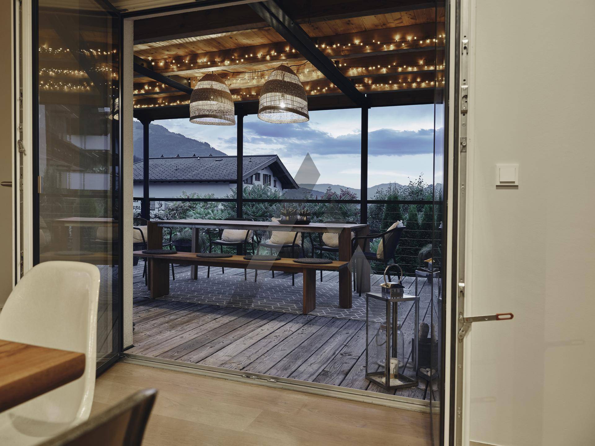 Überdachte Terrasse mit Esstisch, Lichterketten und Blick auf die umliegende Landschaft.
