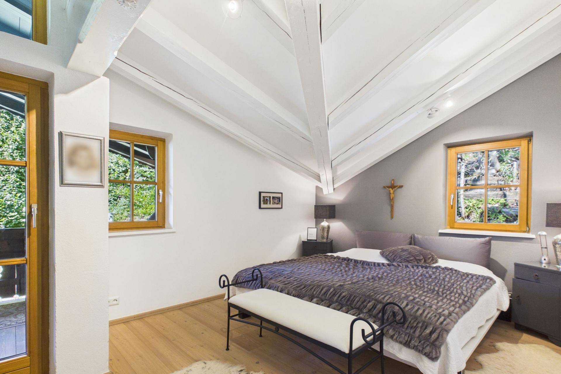 Schlafzimmer im Dachgeschoss mit Doppelbett, sichtbaren Holzbalken und Fenstern mit Bergblick.