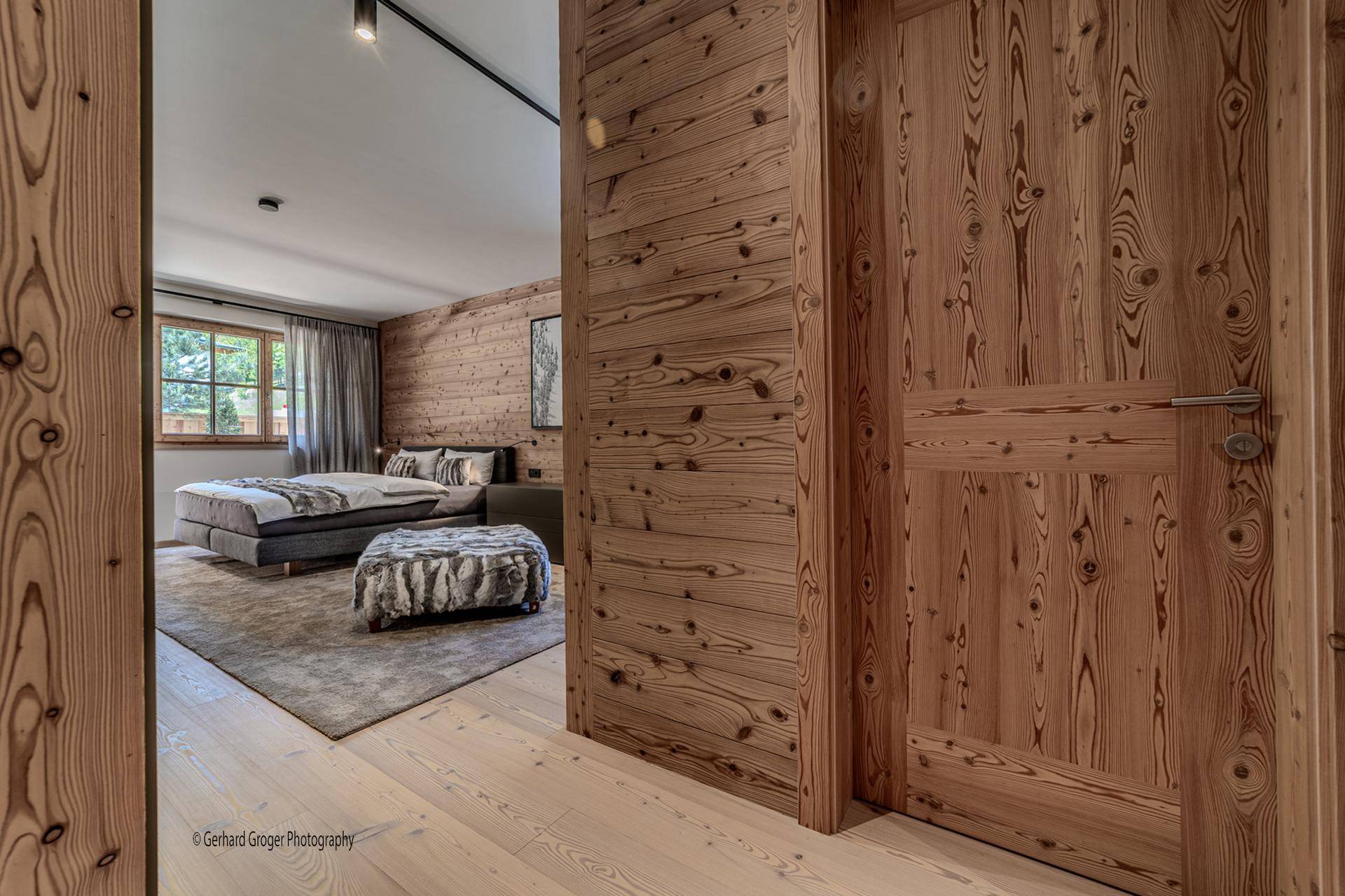 Schlafzimmer mit Holzwand, großem Bett und Blick auf den Flur.