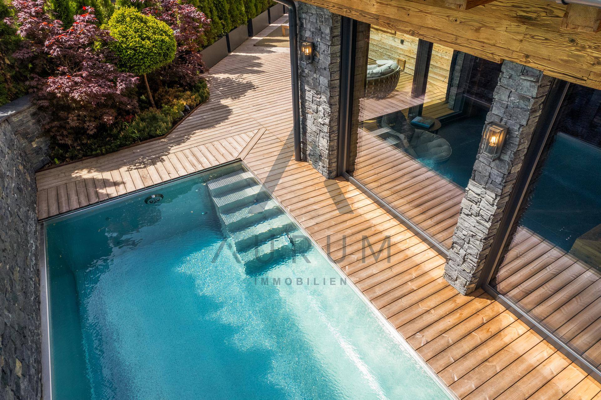 Blick von oben auf den kleinen Pool und die Holzterrasse, umgeben von Steinmauern und Pflanzen.