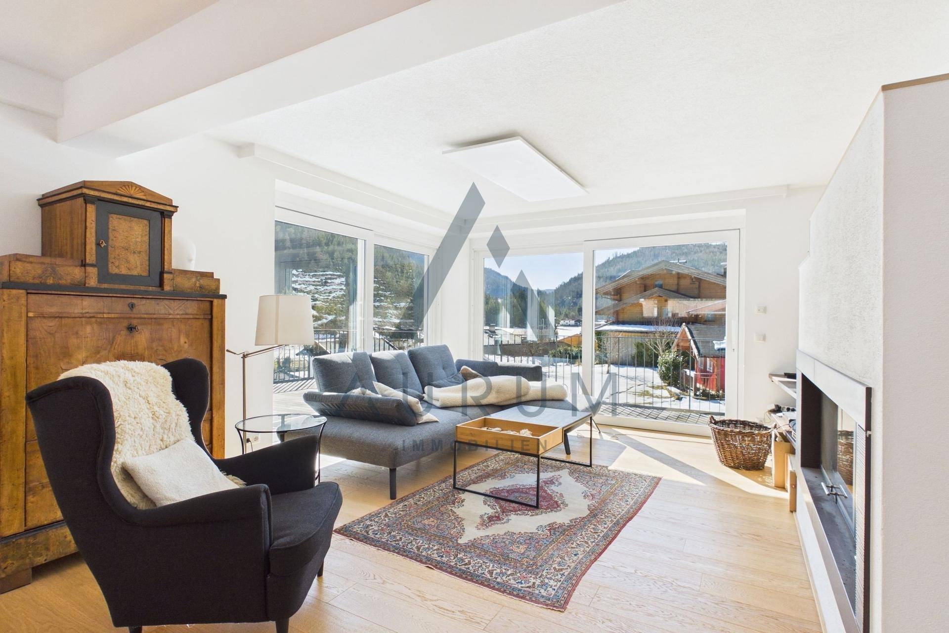 Helles Wohnzimmer mit bequemen Sofas, Kamin und großen Fenstern mit Bergblick.
