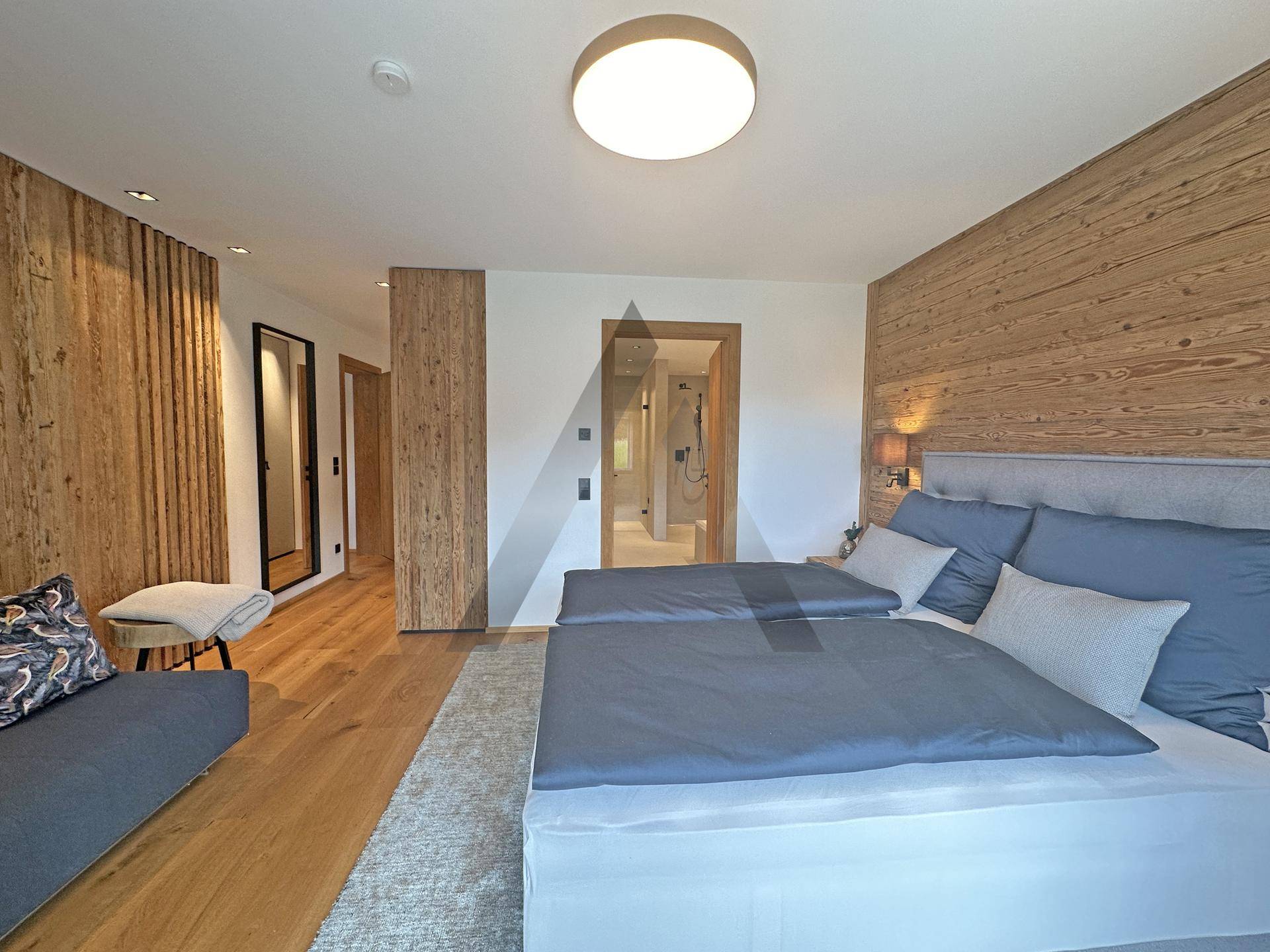 Helles Schlafzimmer mit Holzwänden, Doppelbett und Blick auf den angrenzenden Flur und Bad.