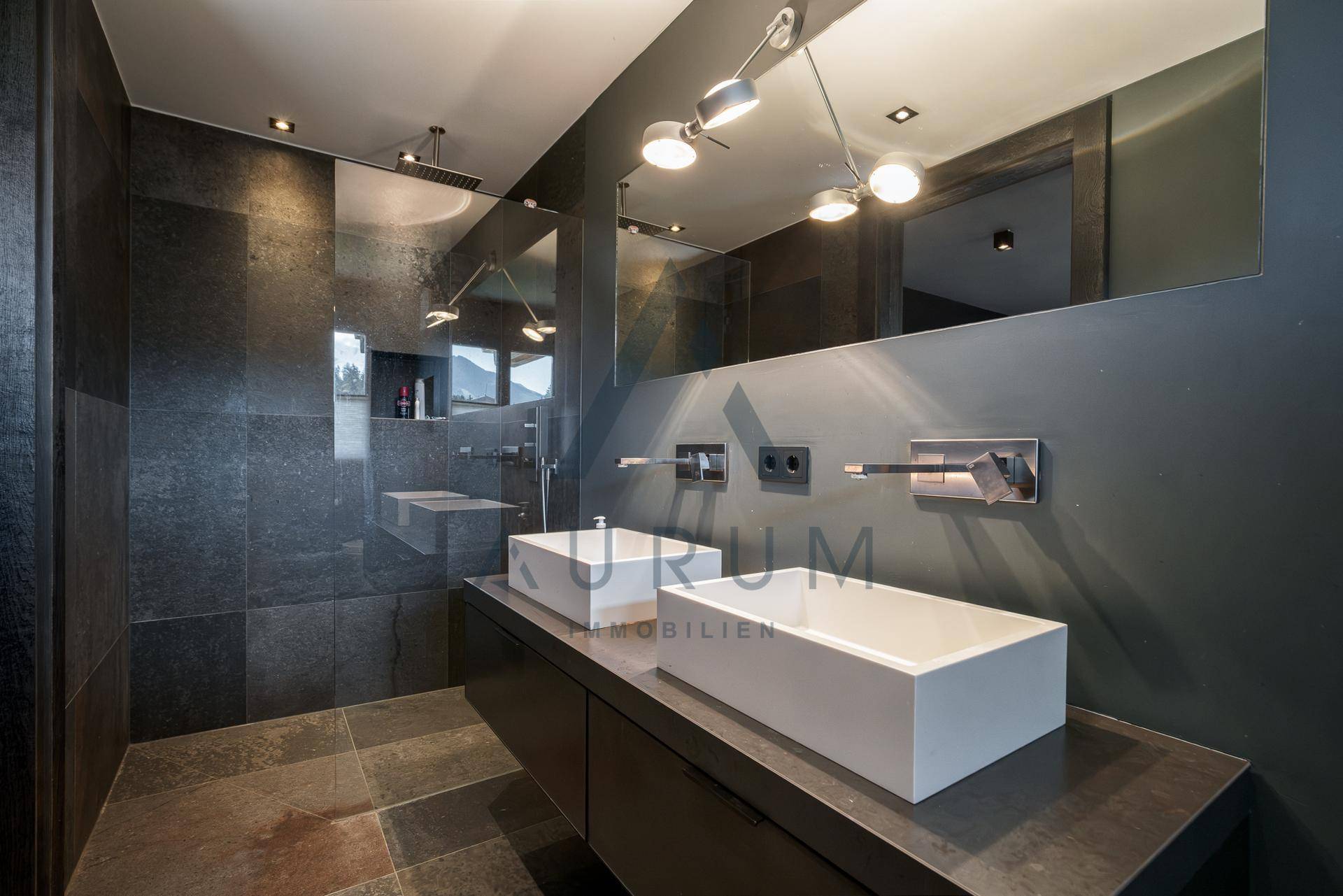 Elegantes Badezimmer mit zwei Aufsatzwaschbecken und großem Spiegel in dunklen Farbtönen.