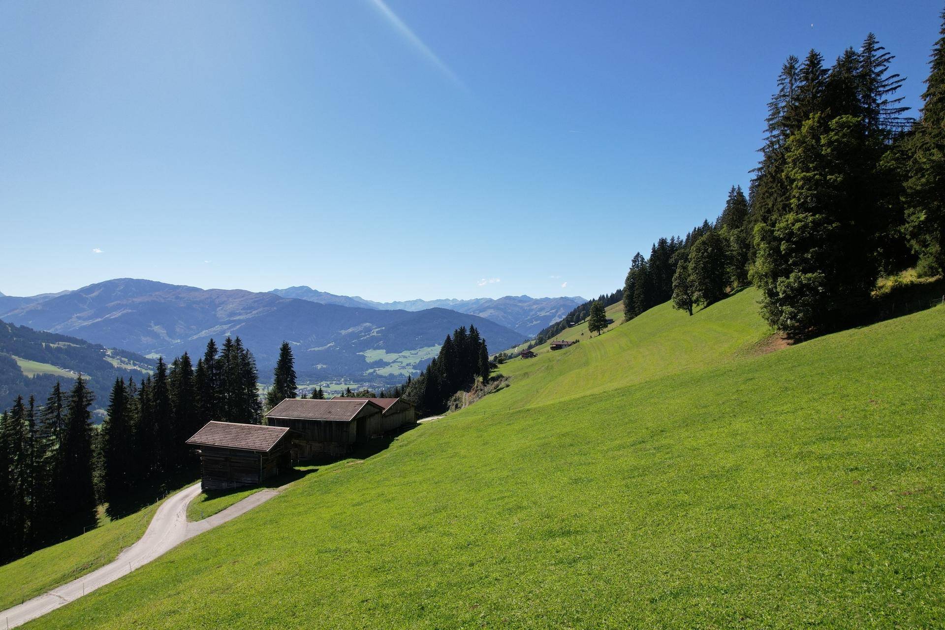 Weitläufige grüne Hügellandschaft mit vereinzelten Hütten und Bergblick.