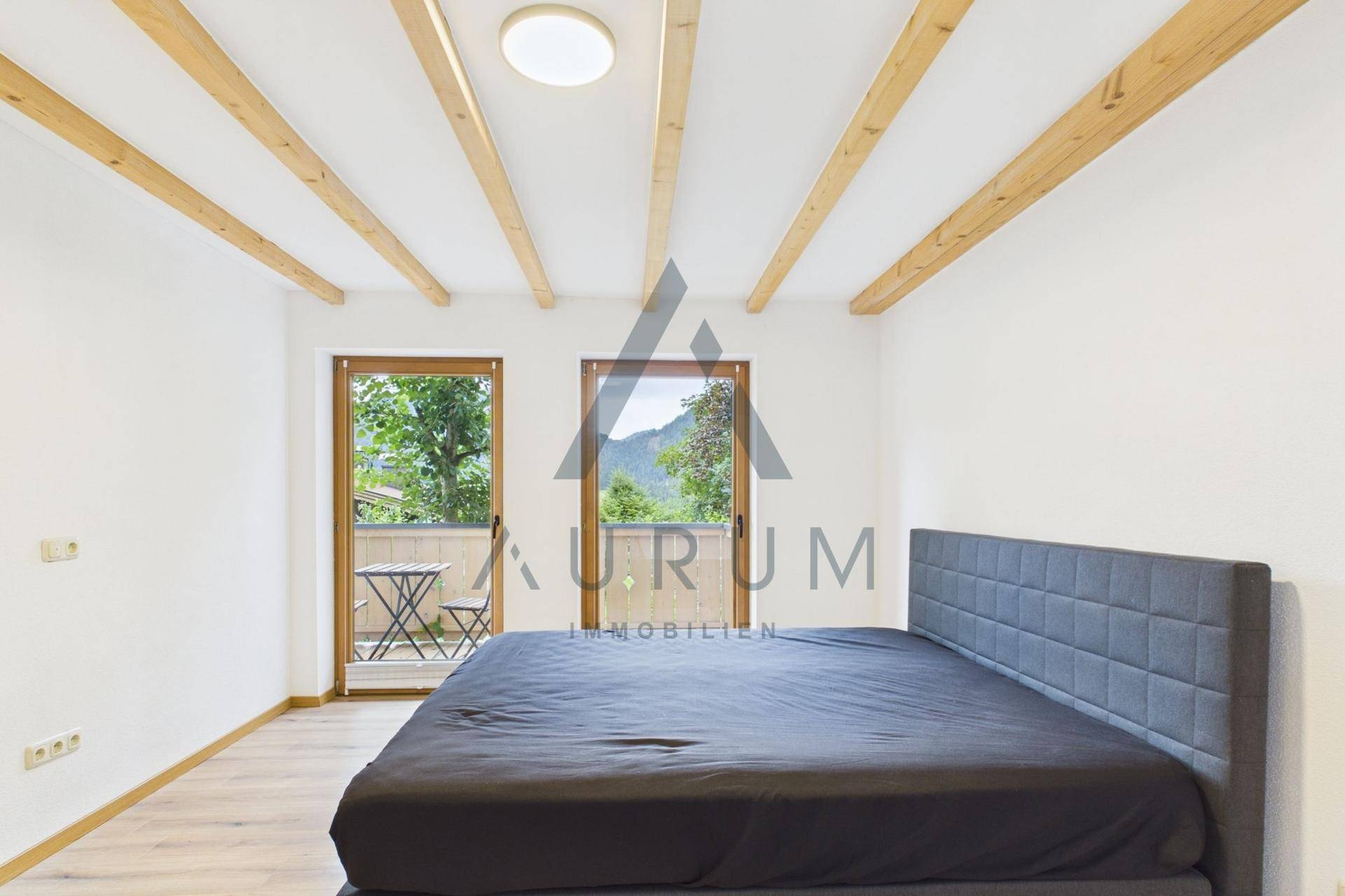 Schlafzimmer mit Holzbalken, großem Bett und Zugang zum Balkon mit Bergblick.