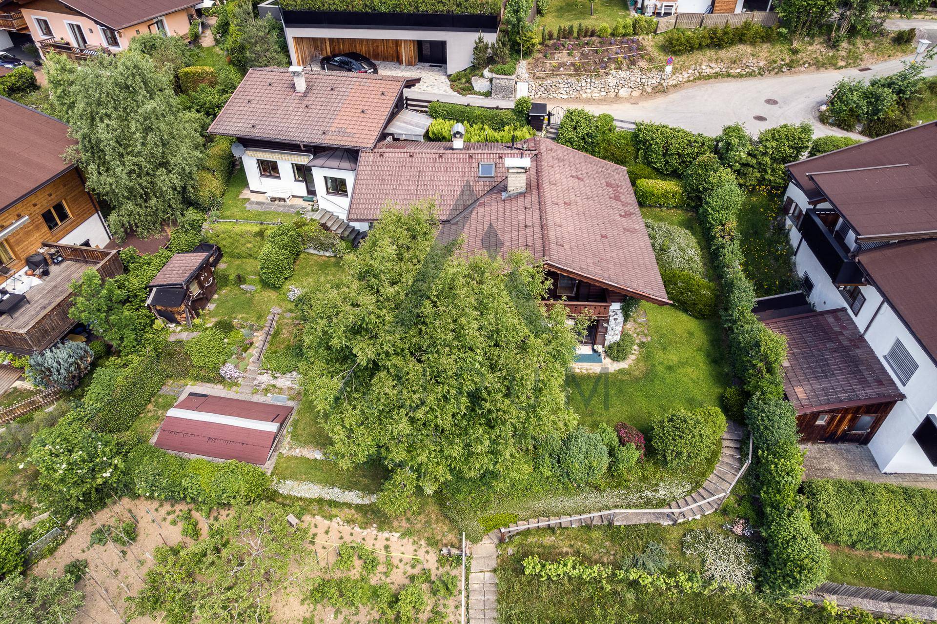 Luftaufnahme eines Anwesens mit großem Garten und umliegenden Häusern in grüner Umgebung.