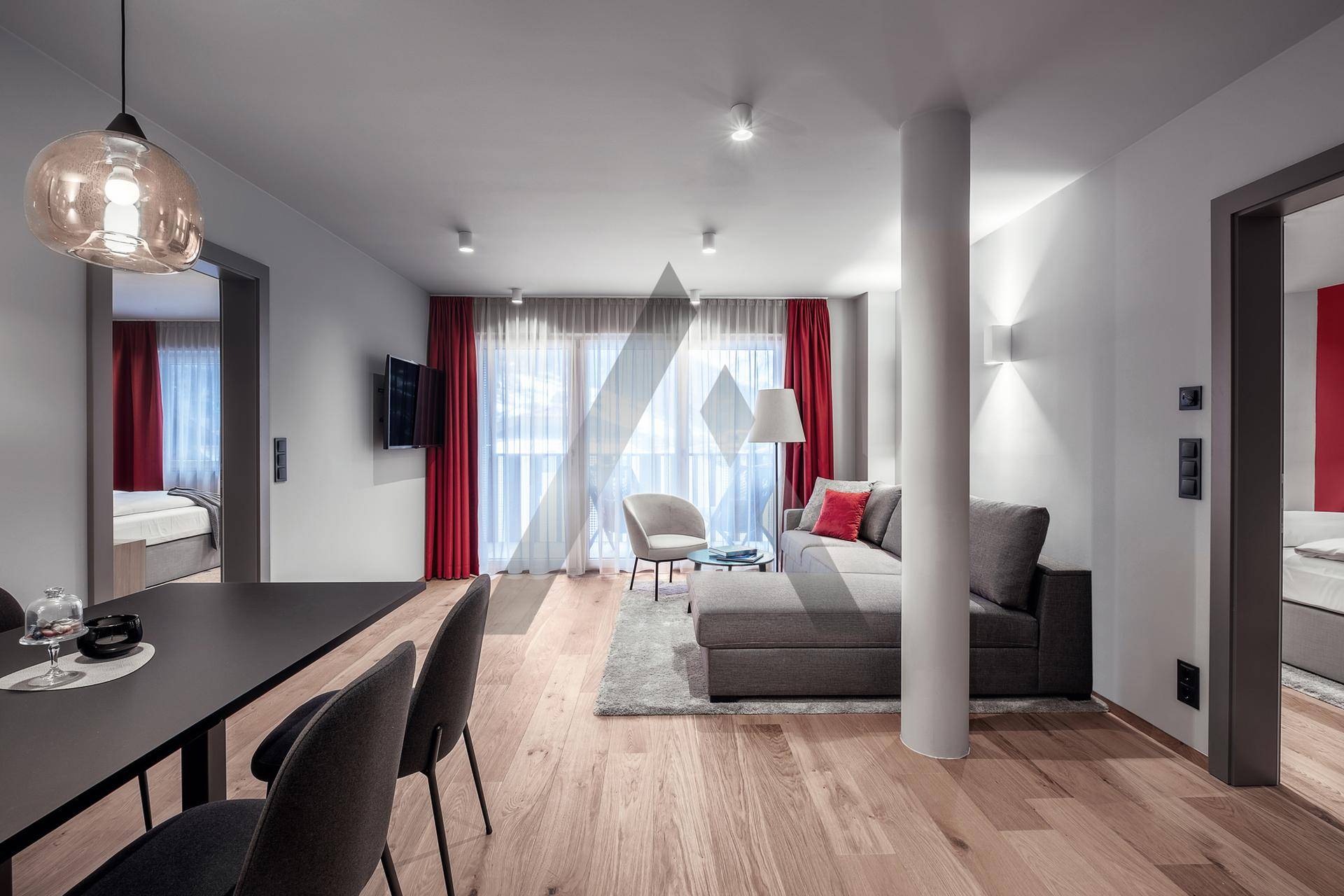 Heller Wohn-Essbereich mit grauem Sofa, Esstisch und roten Vorhängen, ausgestattet mit Holzboden.