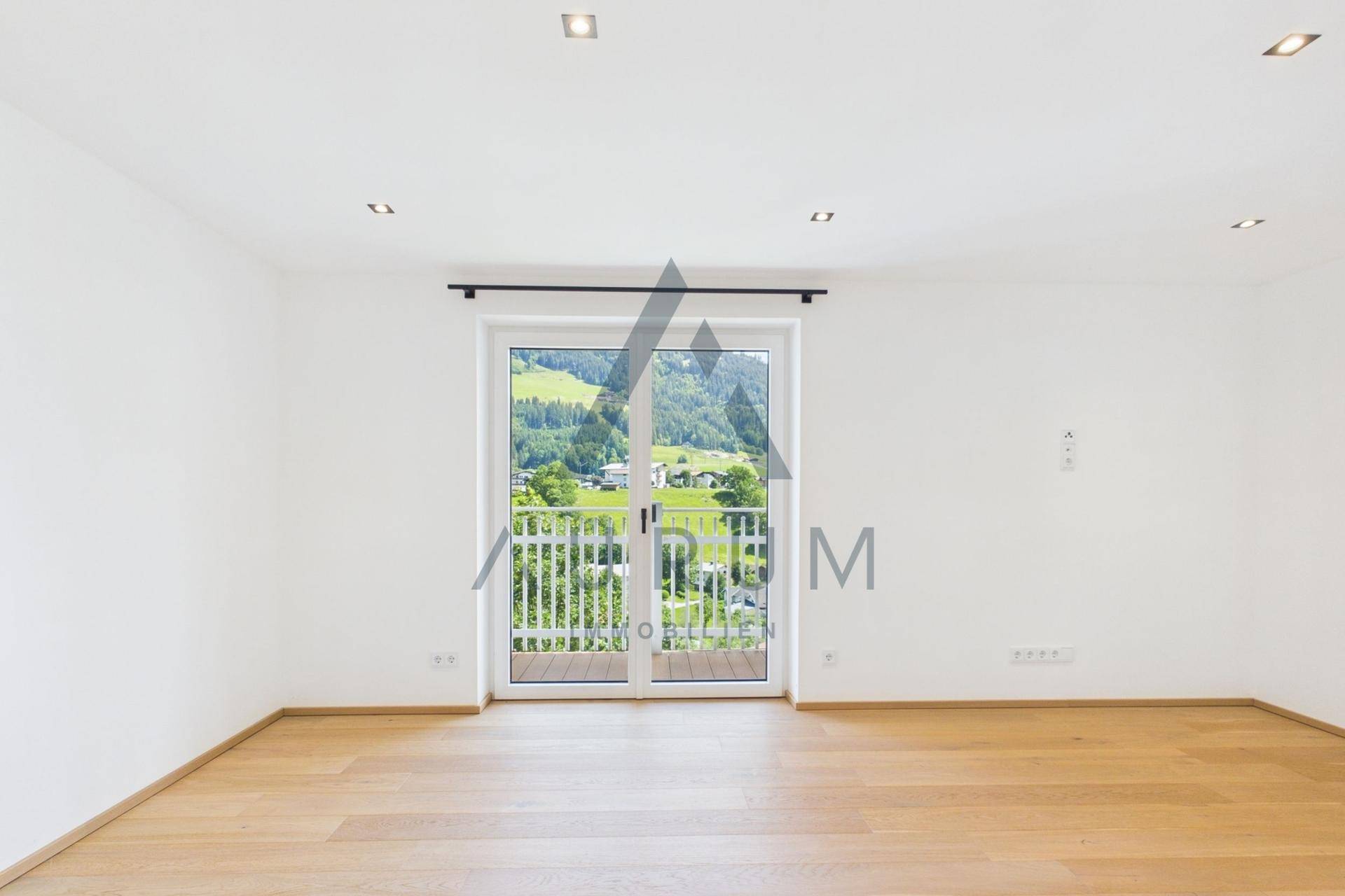 Helles Zimmer mit Holzboden und Zugang zu einem französischen Balkon mit Bergblick.