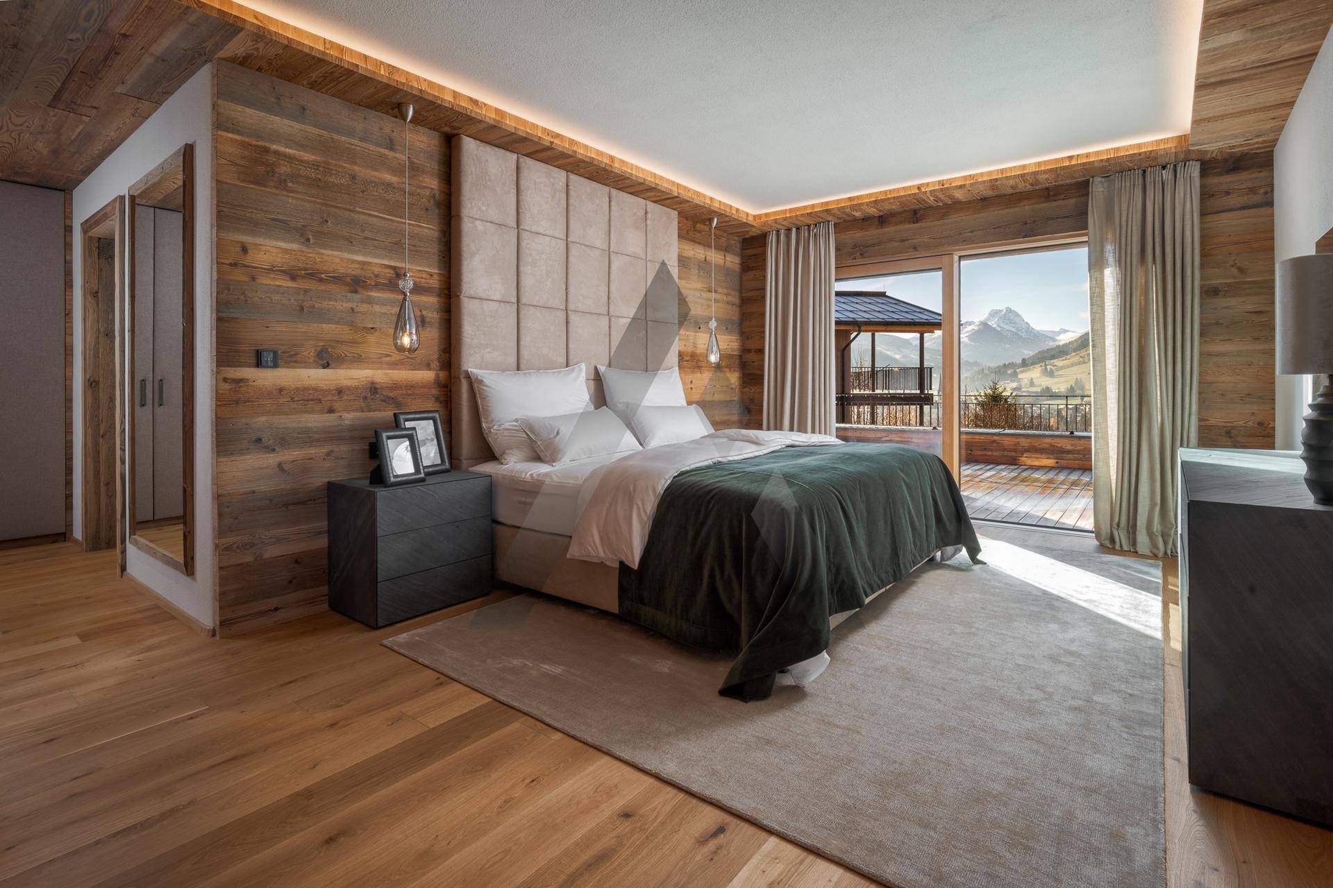 Gemütliches Schlafzimmer mit Holzwänden, gepolstertem Kopfteil und Zugang zu einem Balkon mit Bergblick.