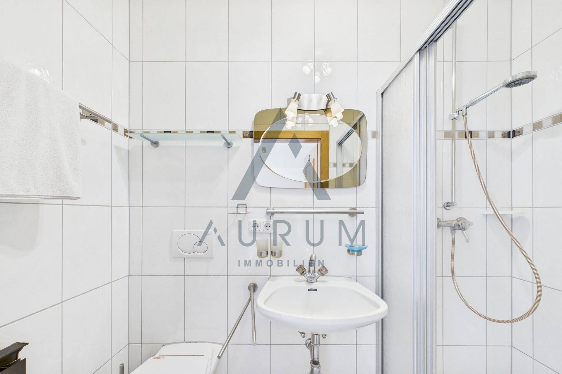 Kleines Badezimmer mit weißen Fliesen, Dusche und Waschbecken.