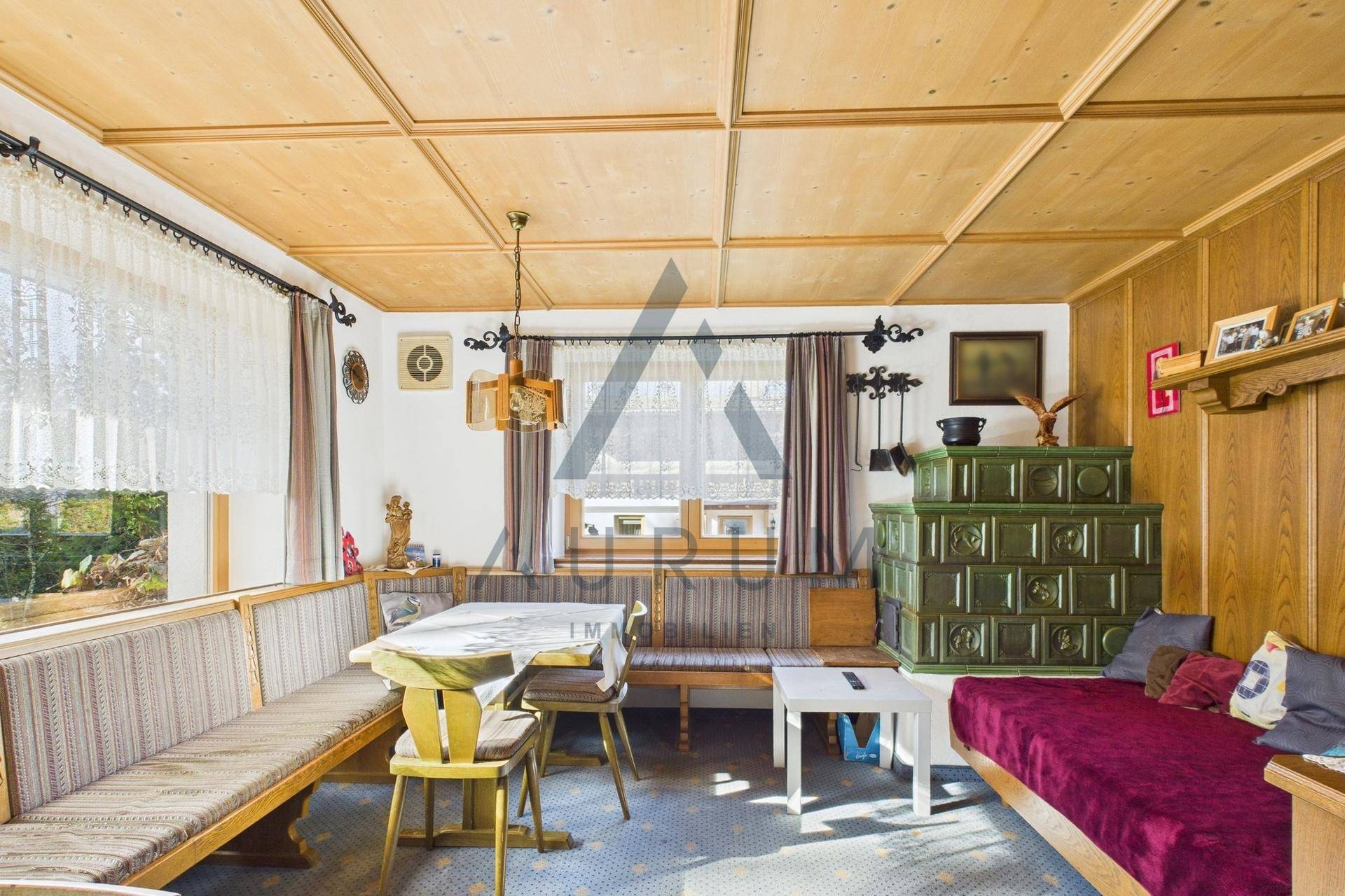 Gemütlicher Wohn-Essbereich im Landhausstil mit Holztäfelung, Kachelofen und traditionellen Möbeln.