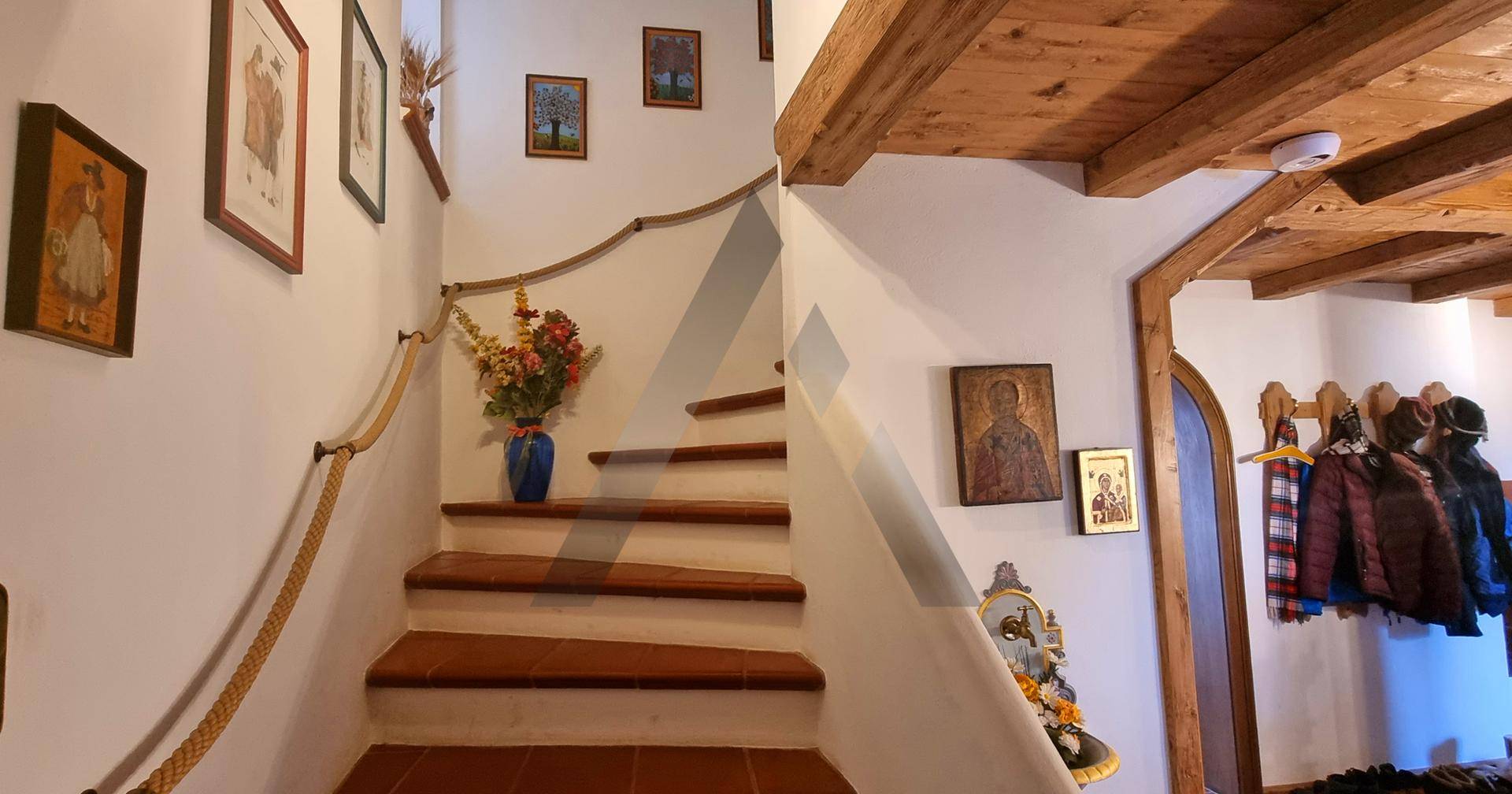 Rustikales Treppenhaus mit Holzstufen, Seilgeländer und traditionellen Bildern an den hellen Wänden.