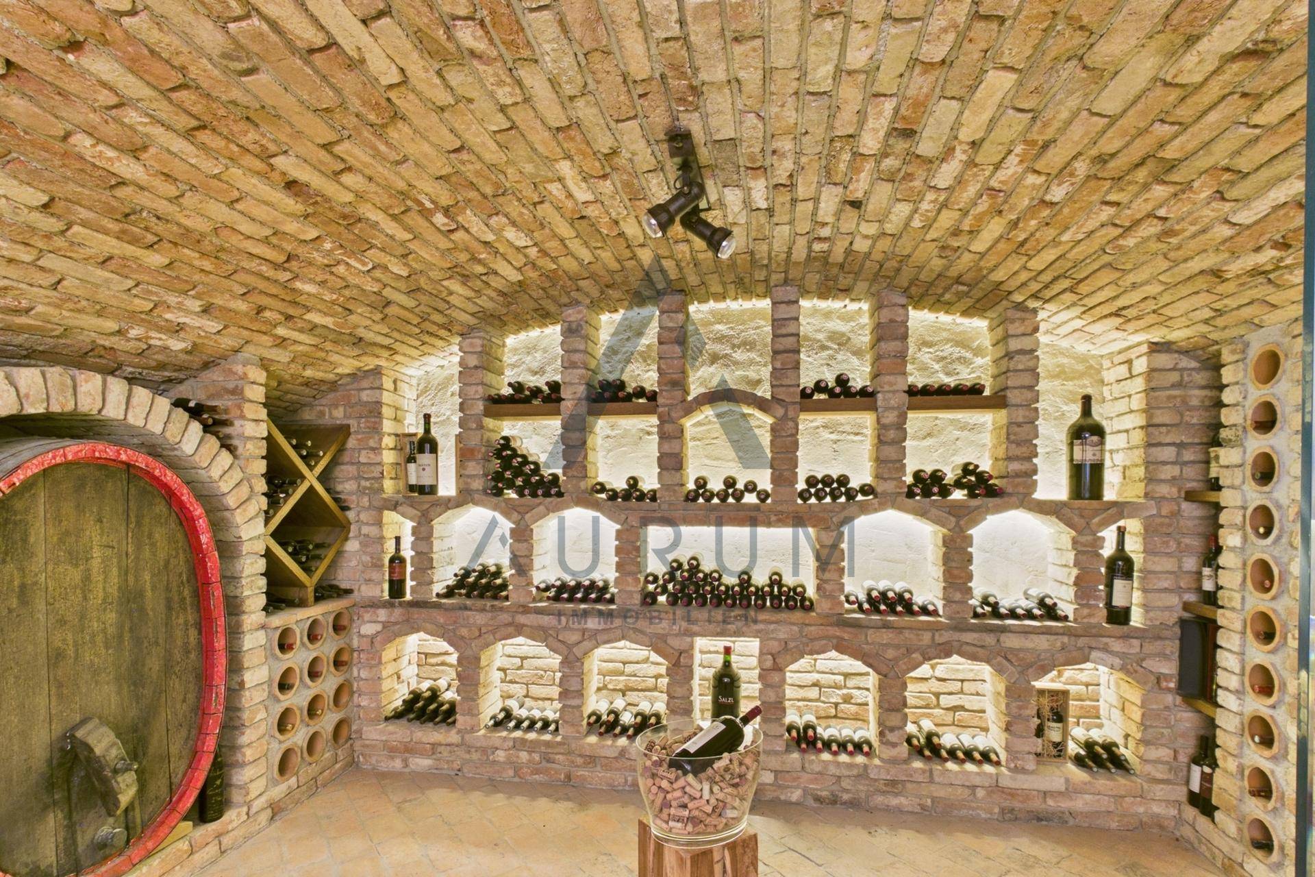 Detailansicht der beleuchteten Weinregale in einem traditionellen Ziegelgewölbekeller mit Weinfässern.