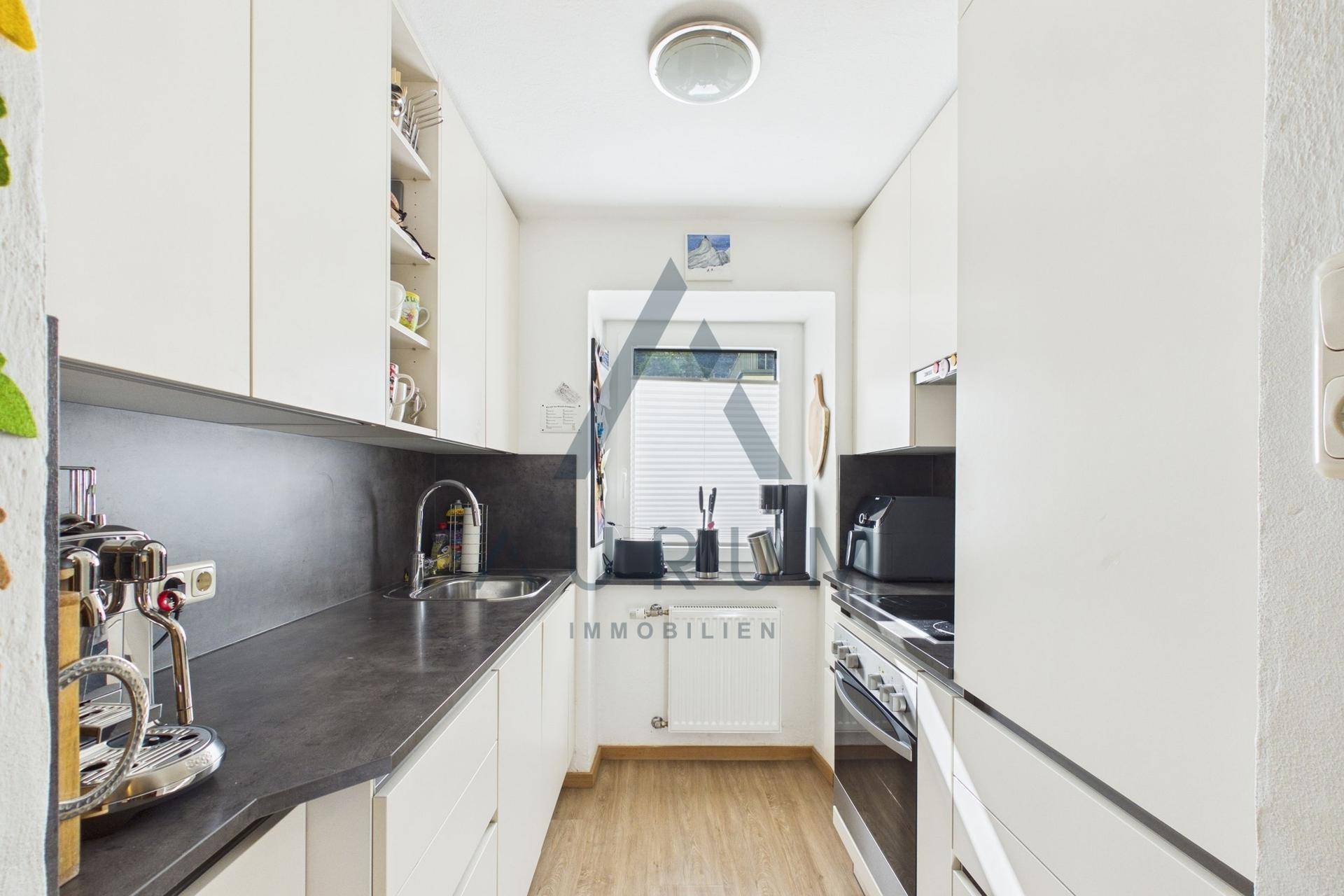 Moderne, schmale Küche mit weißen Schränken, dunkler Arbeitsplatte und Fenster.