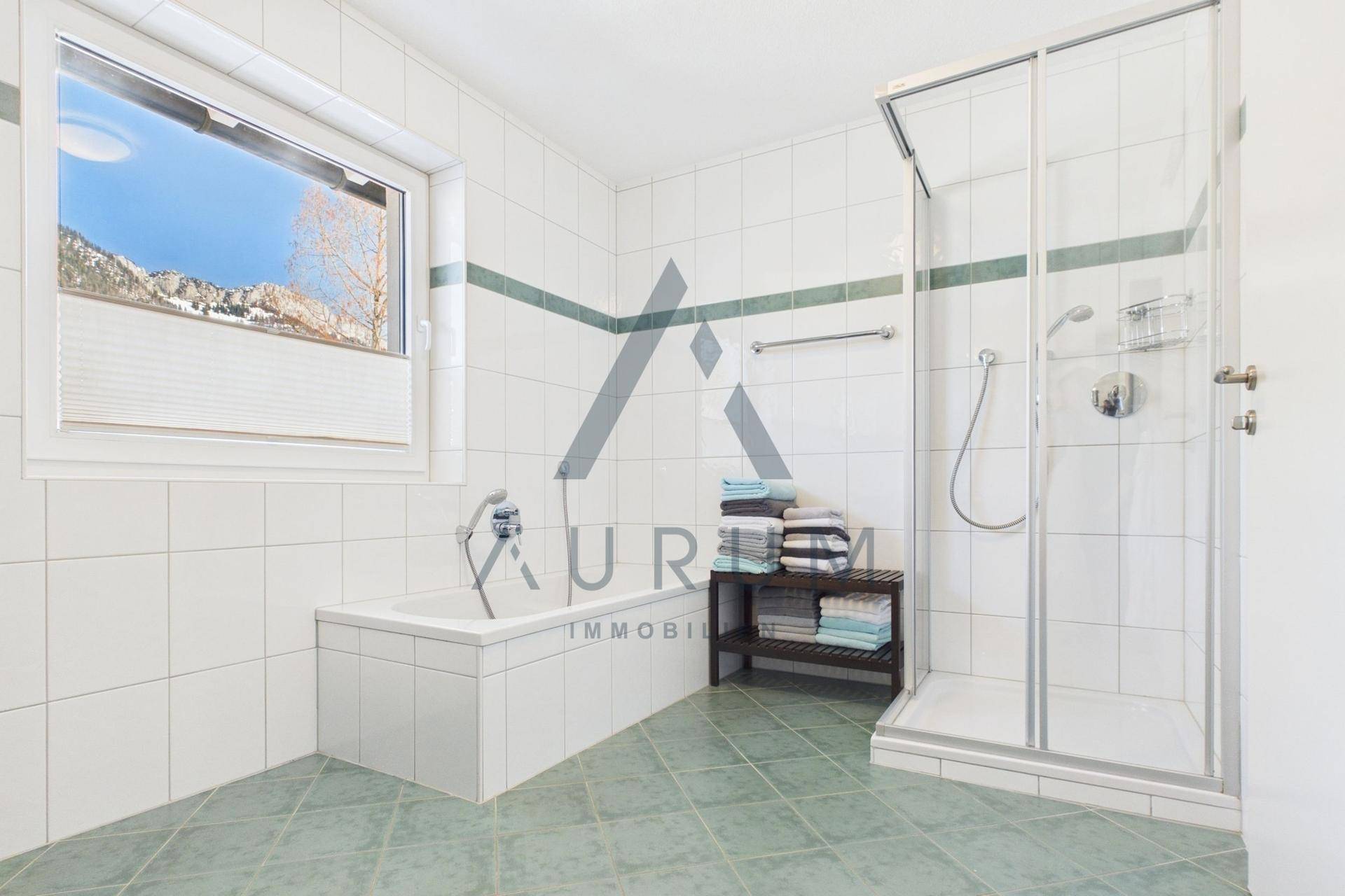 Helles Badezimmer mit Badewanne, Duschkabine und Fenster mit Blick auf die Berge.