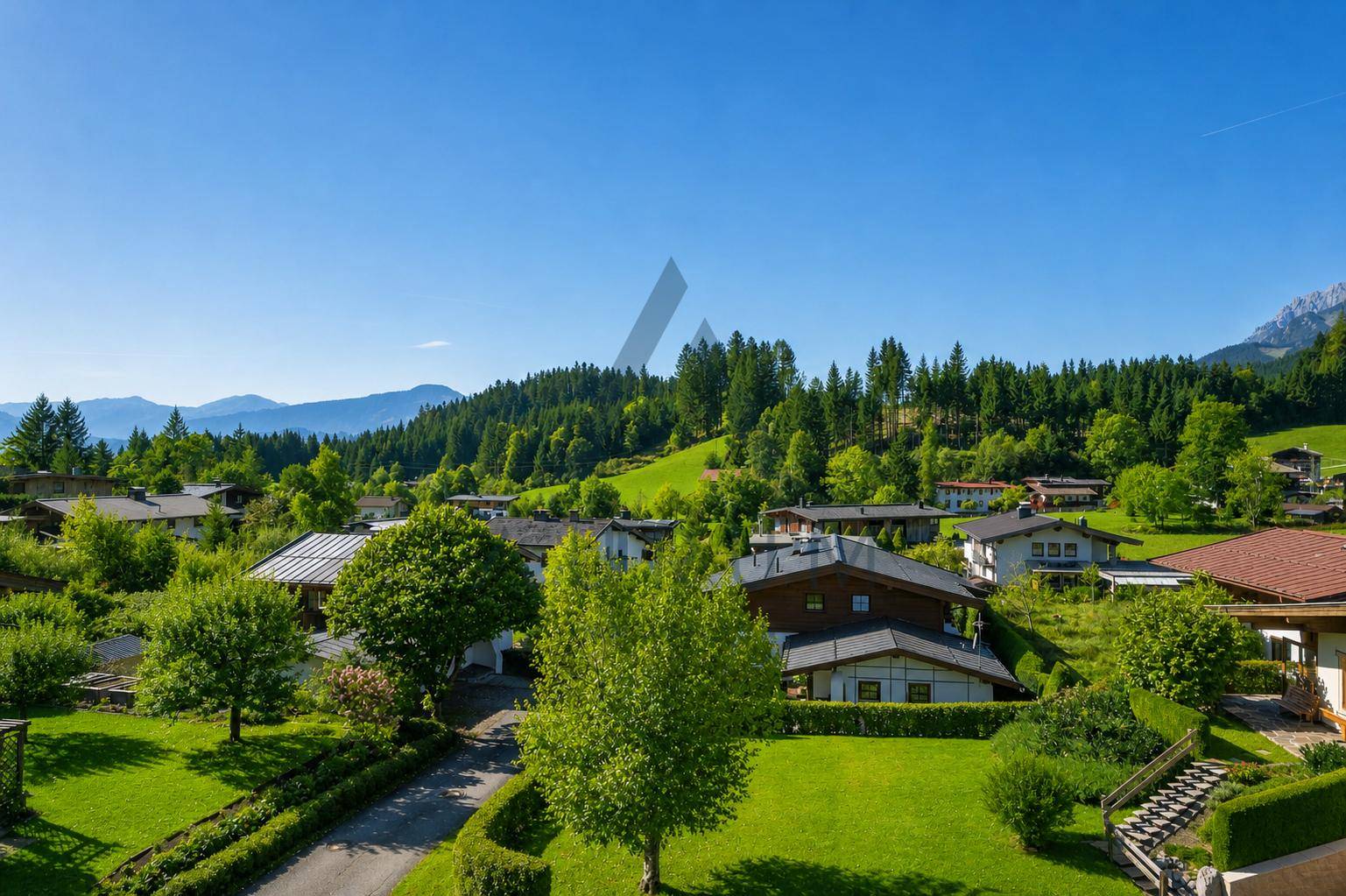 Weitläufige Ansicht einer ländlichen Wohngegend mit vielen Grünflächen und Bergen im Hintergrund.