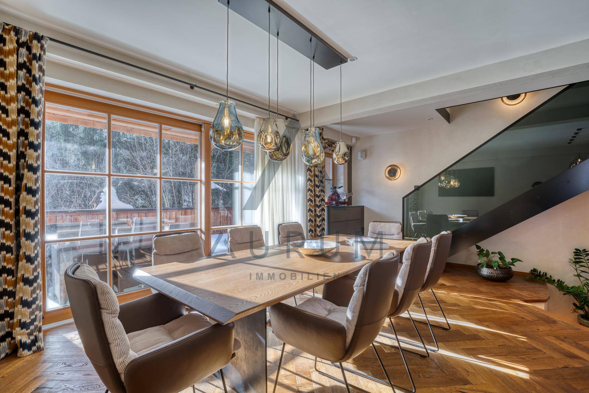 Eleganter Essbereich mit Holztisch, modernen Pendelleuchten und Blick ins Grüne durch große Fenster.