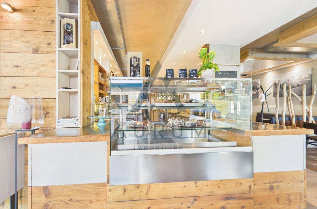 Eine gläserne Kuchentheke präsentiert eine Auswahl an Gebäck und Kuchen in einem Café mit Holzelementen.