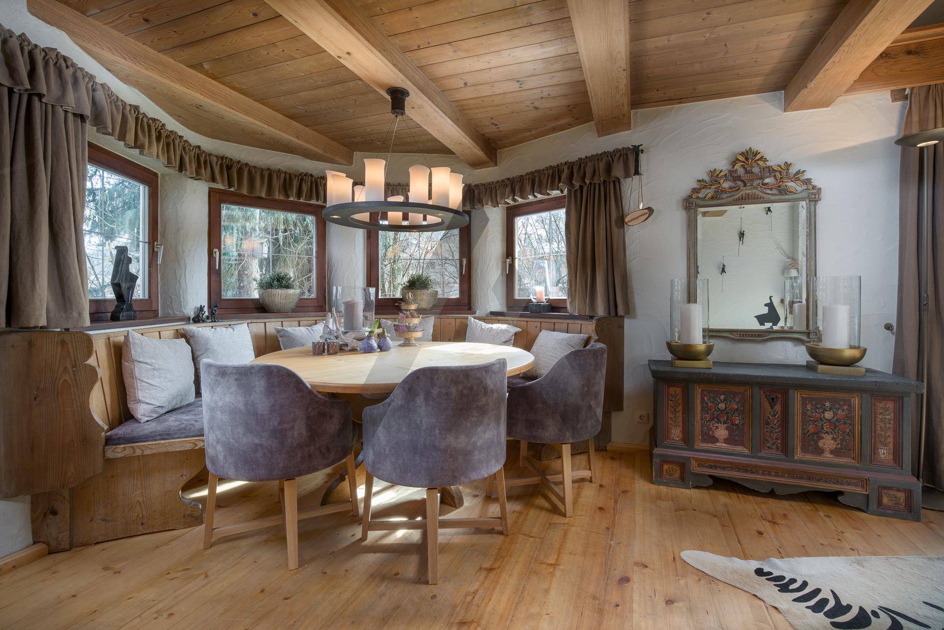 Heller Essbereich mit Holzboden, runder Sitzbank und traditionellem Schrank unter Holzbalken.