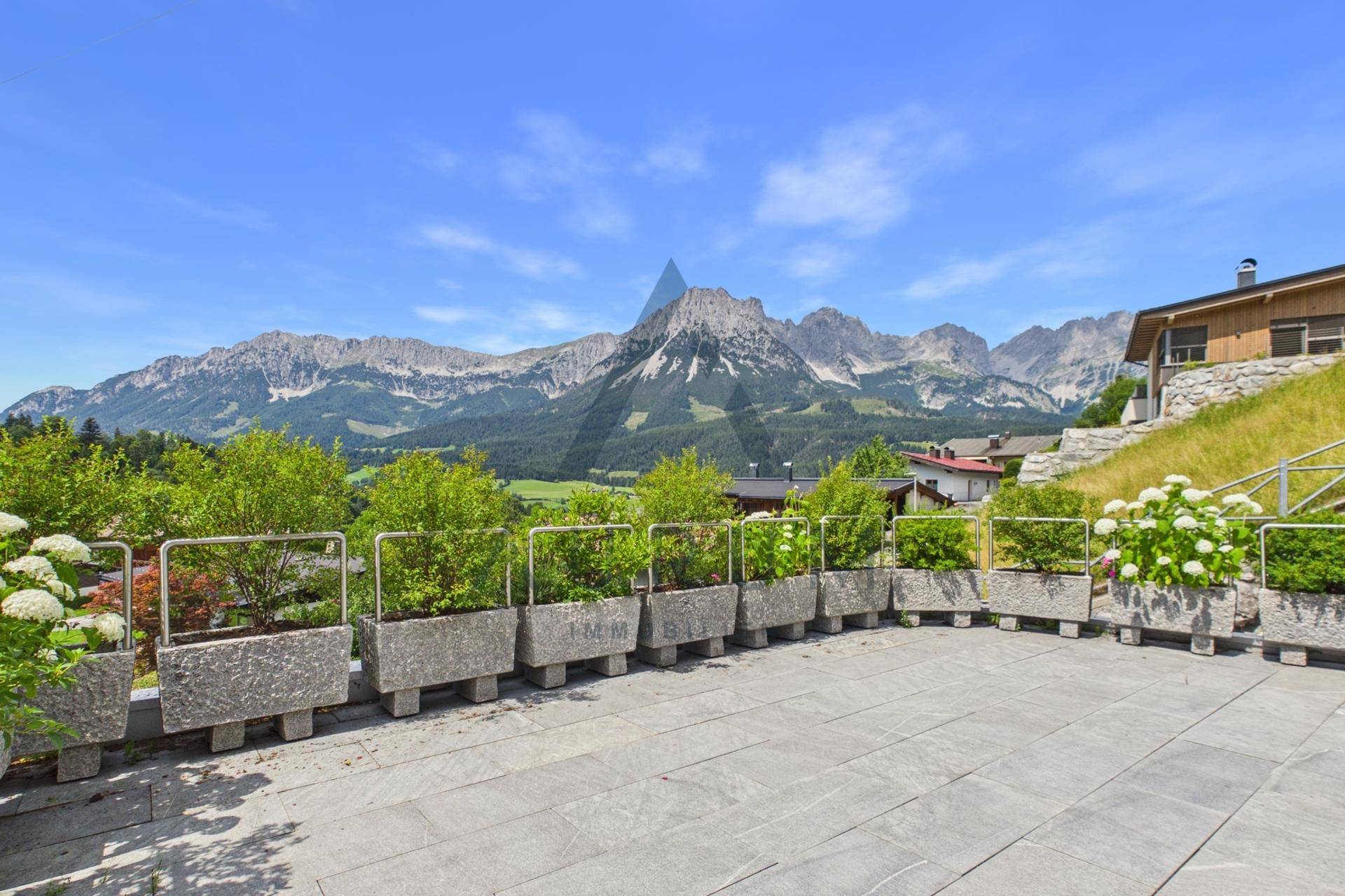 Große Steinterrasse mit Pflanzenkübeln und beeindruckendem Panoramablick auf die Berge.