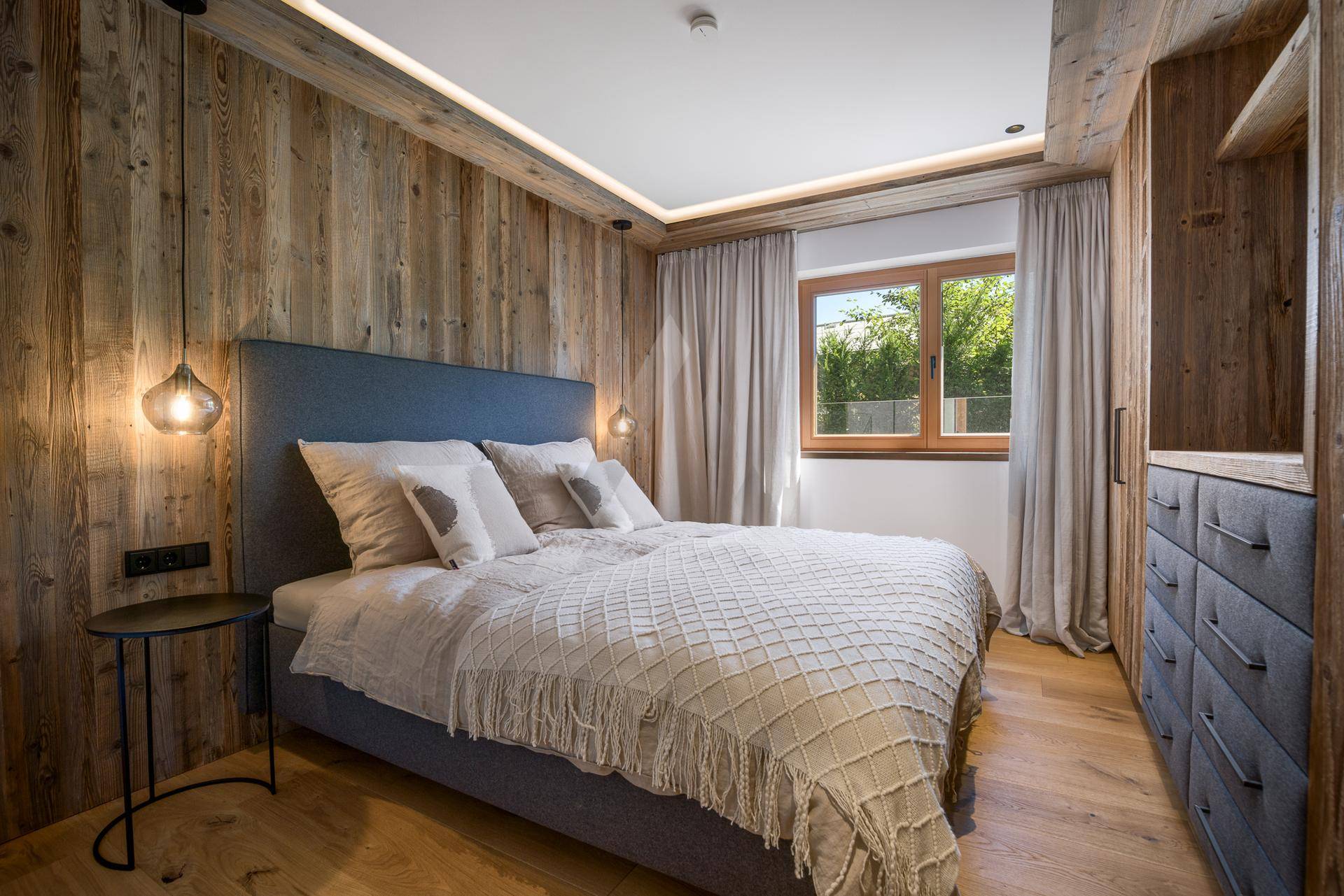 Komfortables Schlafzimmer mit Holzwänden, Holzboden und Fenster mit Grünblick.