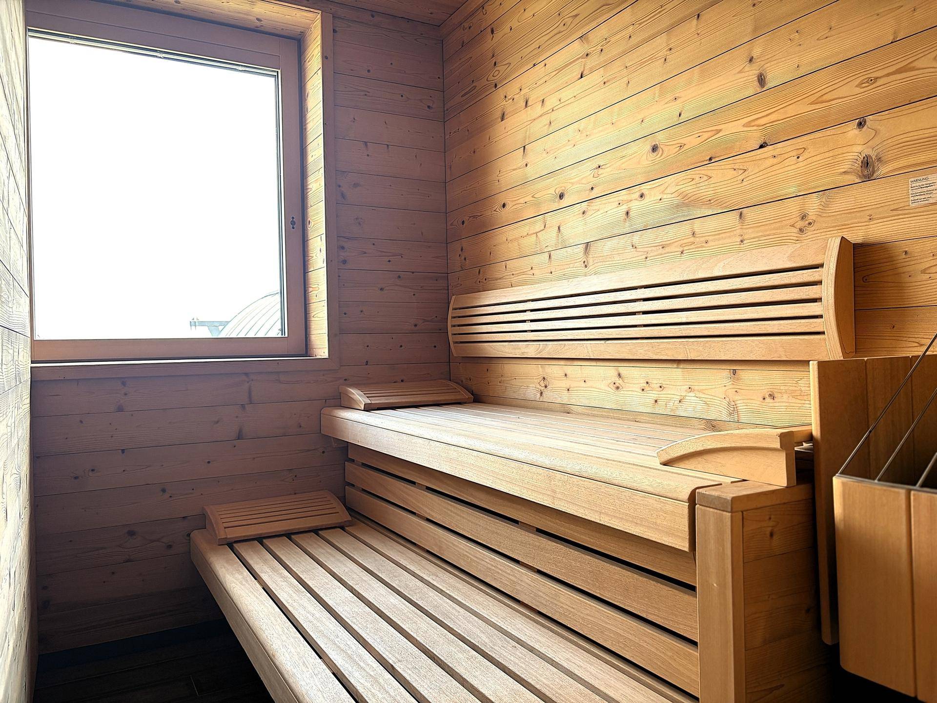 Helle Holzsauna mit bequemen Bänken und einem Fenster für natürliches Licht.