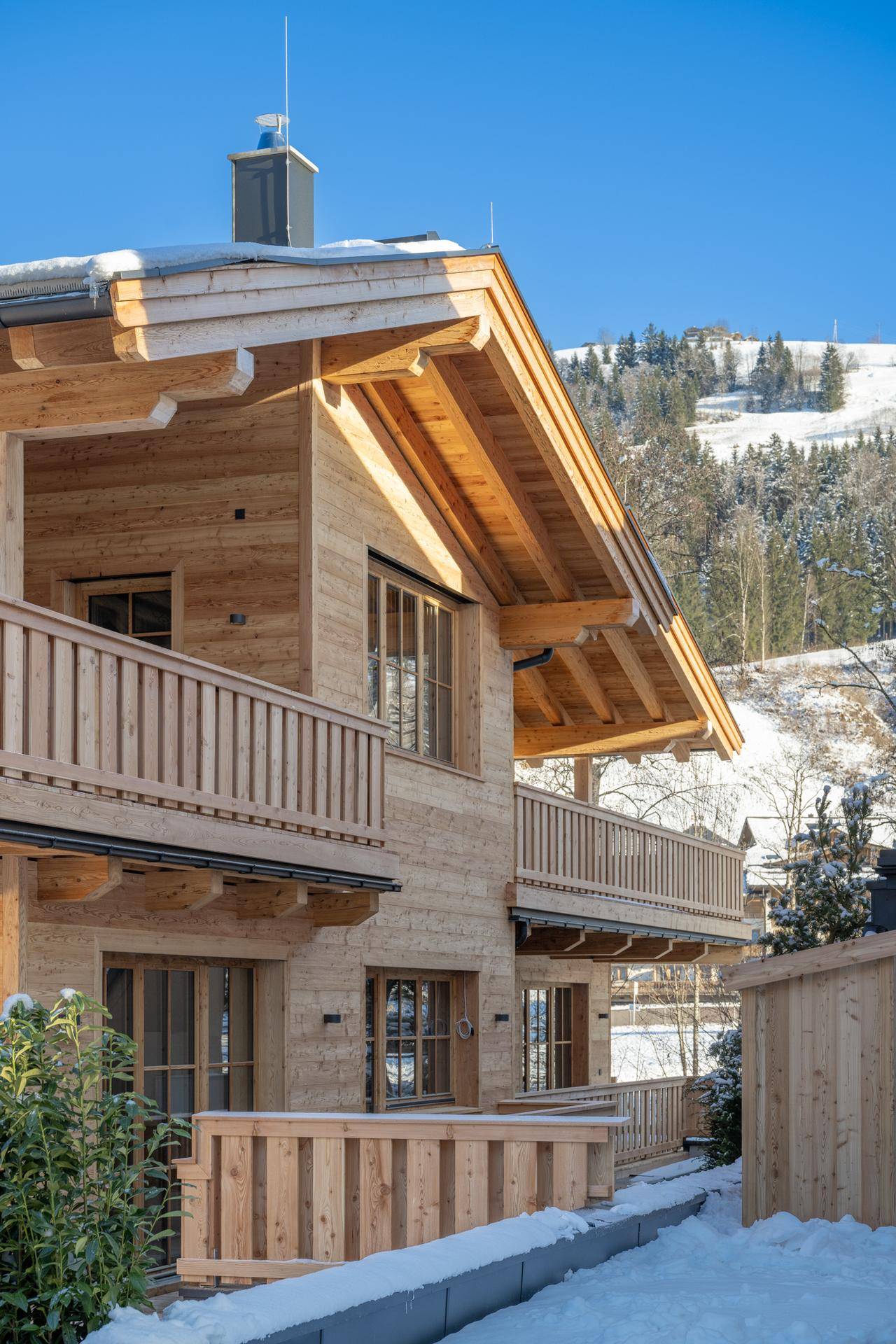 Modernes Holzchalet mit traditionellen Balkonen und Blick auf die verschneiten Berge.