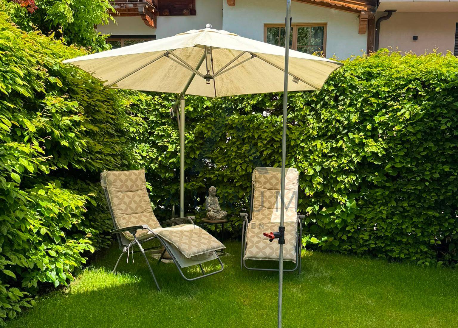Entspannender Gartenbereich mit Liegestühlen, Sonnenschirm und gepflegtem Rasen.