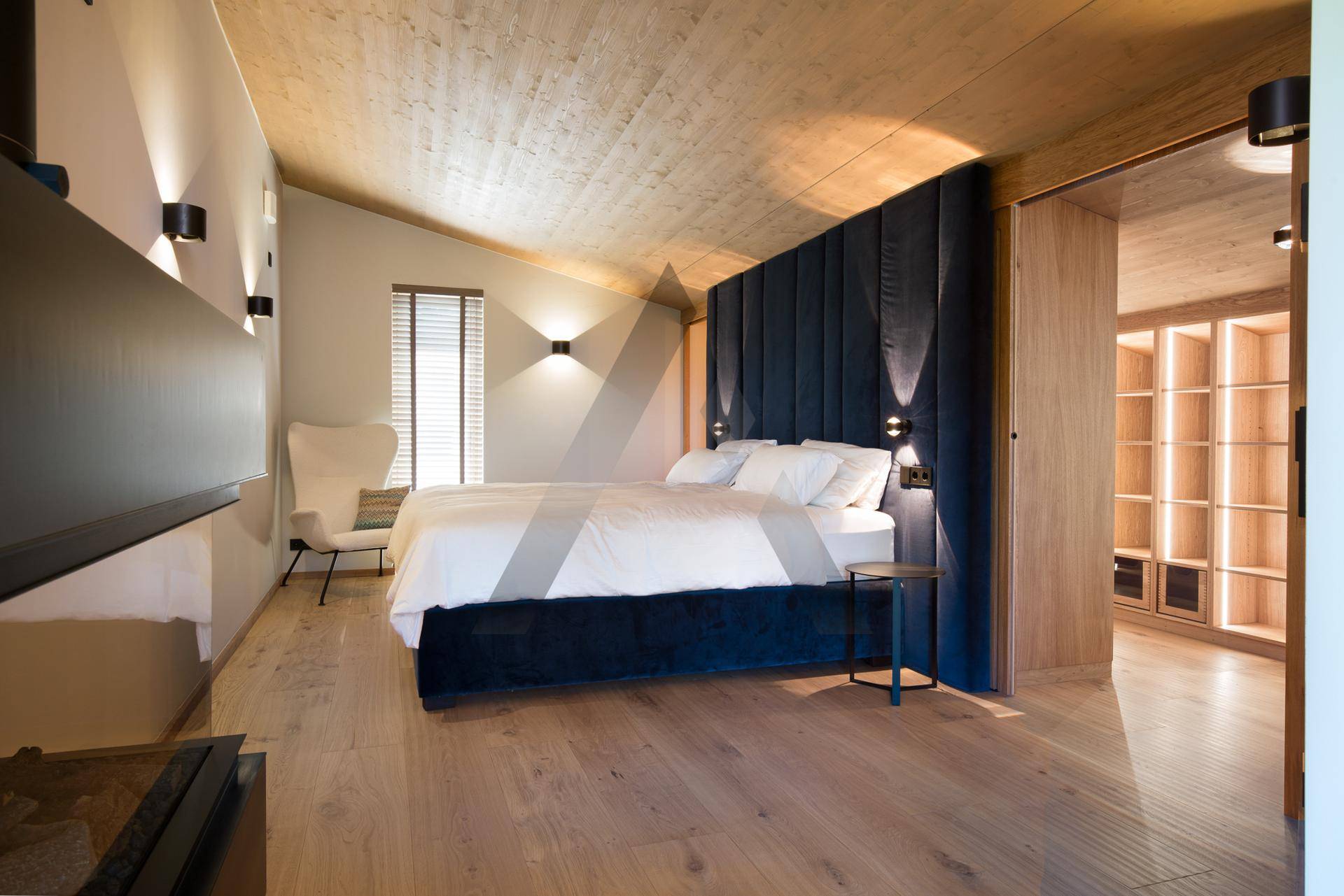 Elegantes Schlafzimmer mit Holzboden, gepolstertem Kopfteil und angrenzendem begehbarem Kleiderschrank.